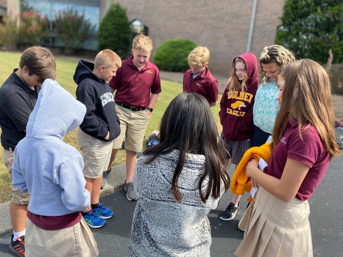 Group of students in school uniforms huddled together, praying outside.