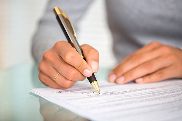 Person's hand writing on a paper with a black and gold pen. Close-up shot on a clear desk.