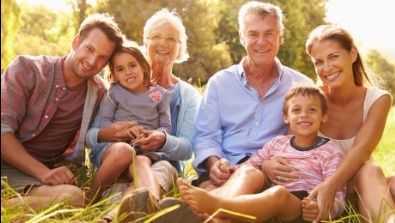 Family of seven smiling together outdoors in grass.