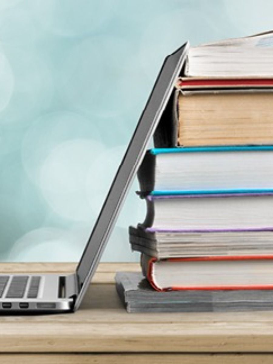Laptop propped against a stack of colorful books on a wooden surface, soft background.