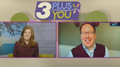 A woman and a man on a virtual TV show set. They are smiling. The logo