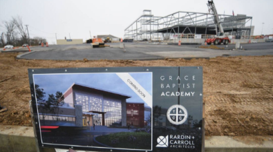 Construction site of Grace Baptist Academy with a sign showing the planned building design.