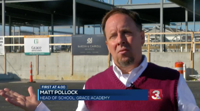 Matt Pollock, head of school at Grace Academy, speaks in front of a construction site. He wears a maroon vest.