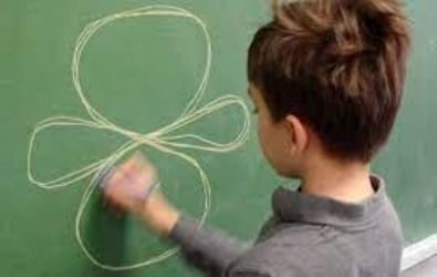 Boy drawing an infinity-shaped figure on a green chalkboard with white chalk.