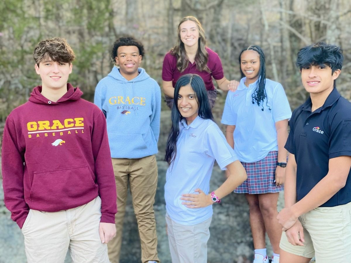 Group of six diverse students standing on rocks; some smiling.