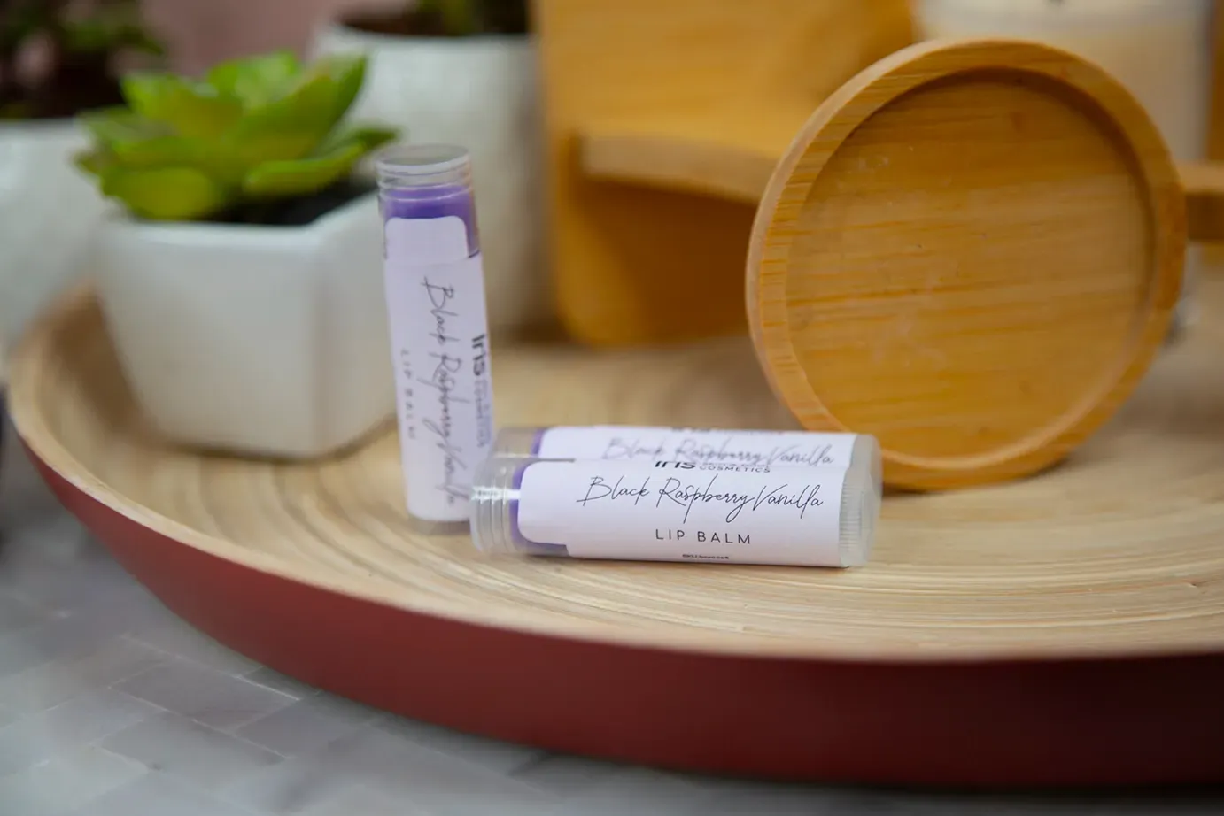 Two bottles of lip balm are sitting on a wooden tray.