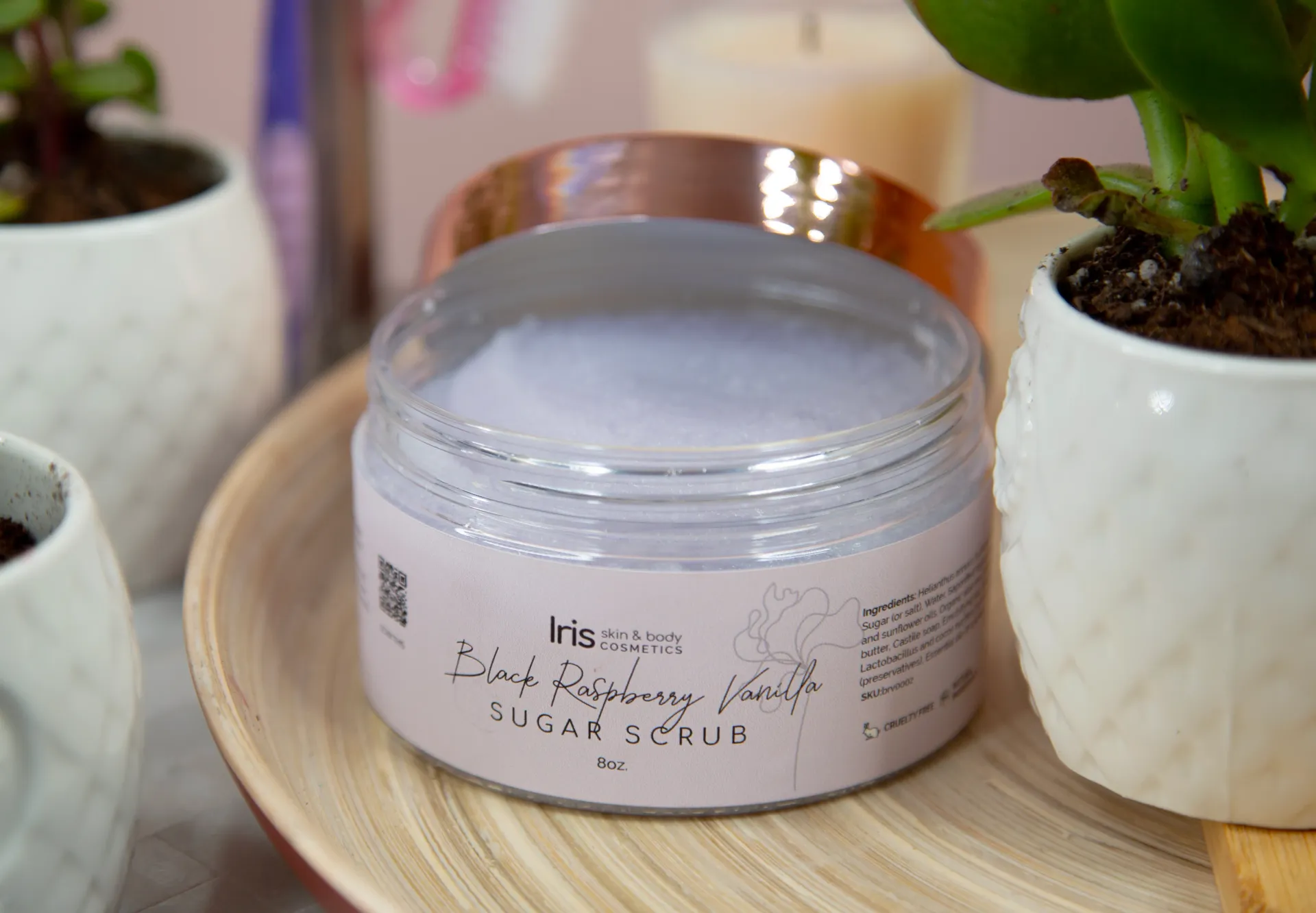 A jar of purple powder is sitting on a wooden plate next to potted plants and candles.