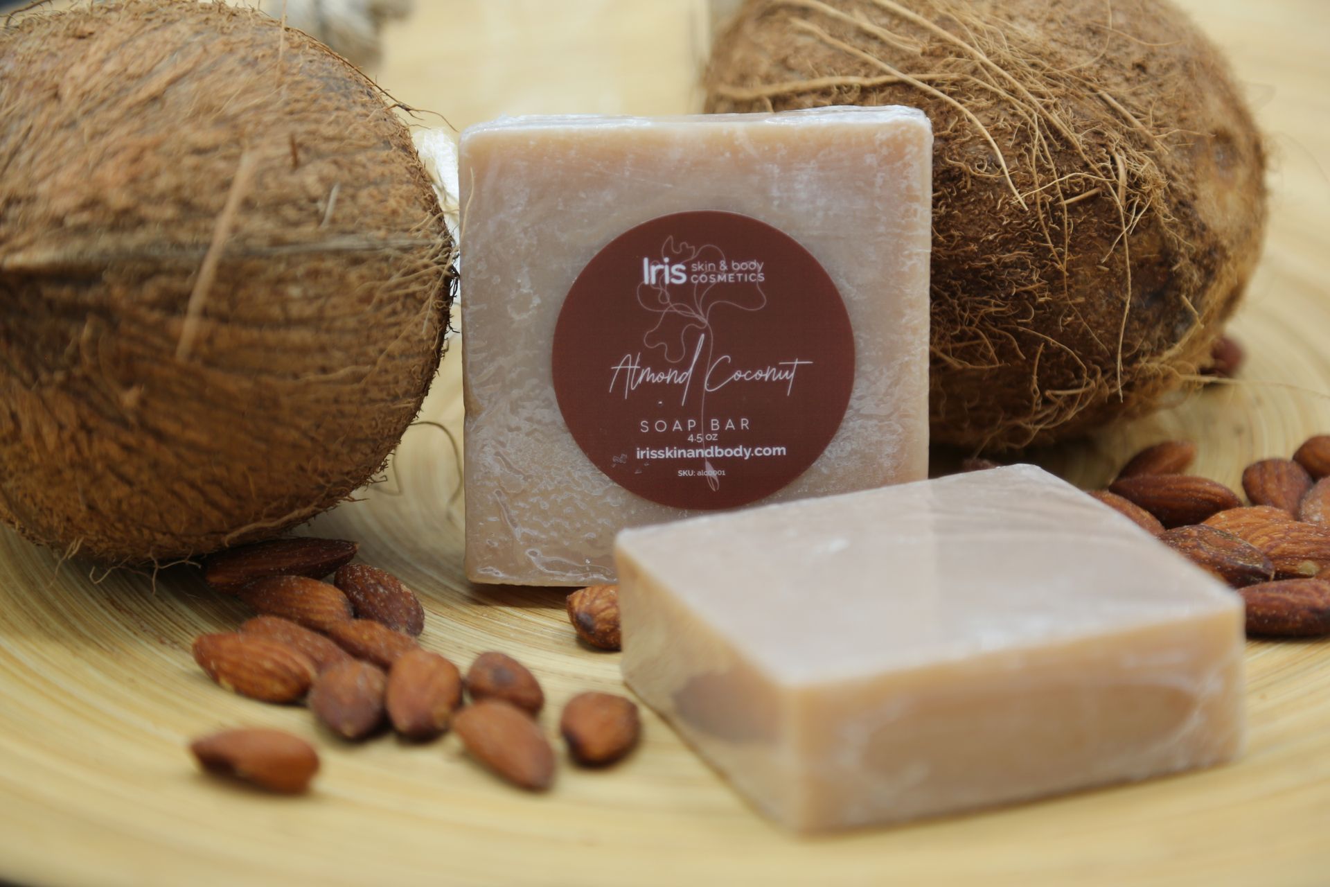 A bar of soap is sitting on a wooden table next to coconuts and almonds.