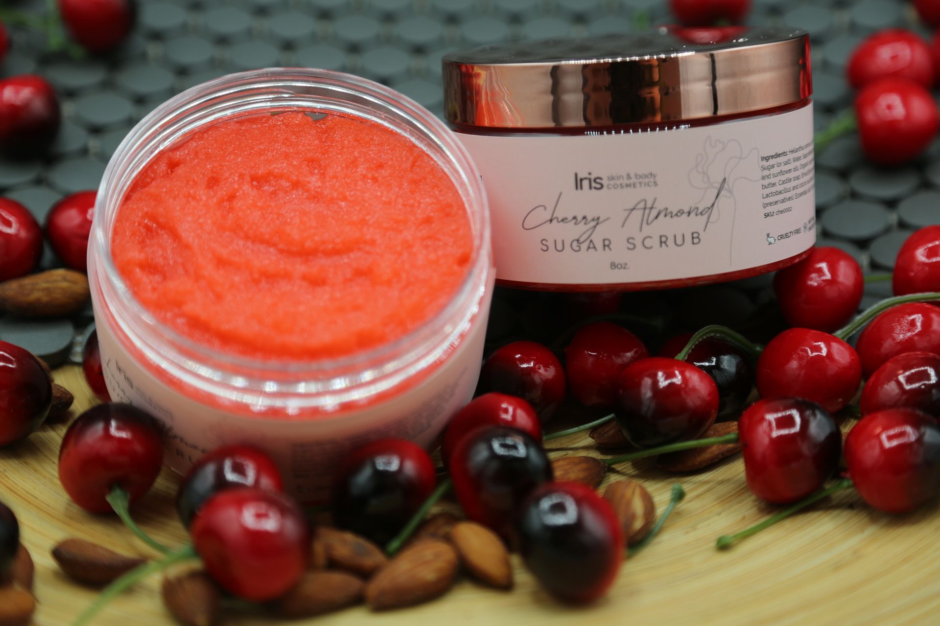 A jar of cherry almond sugar scrub is surrounded by cherries and almonds.