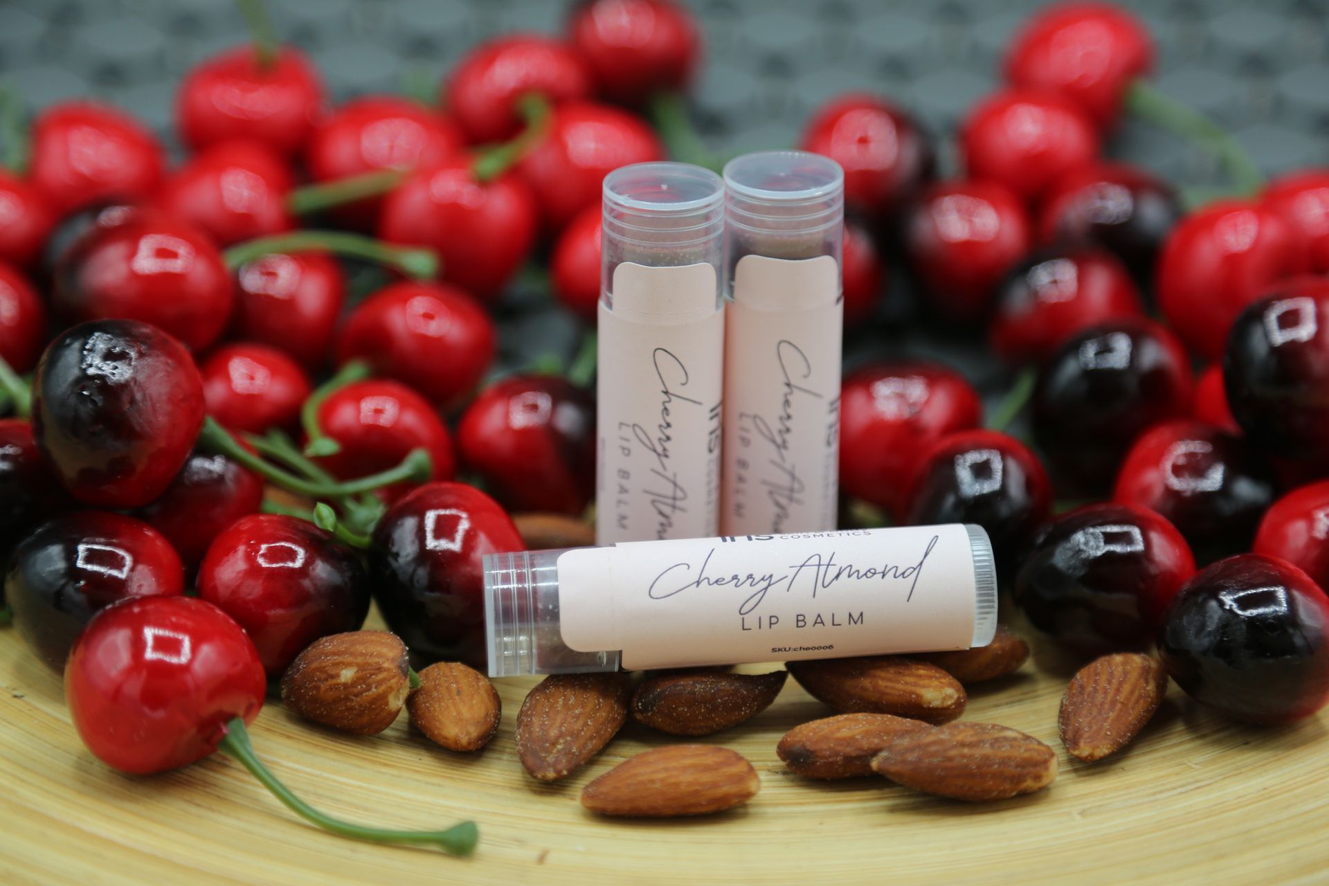 Two tubes of lip balm are sitting on top of a table next to cherries and almonds.