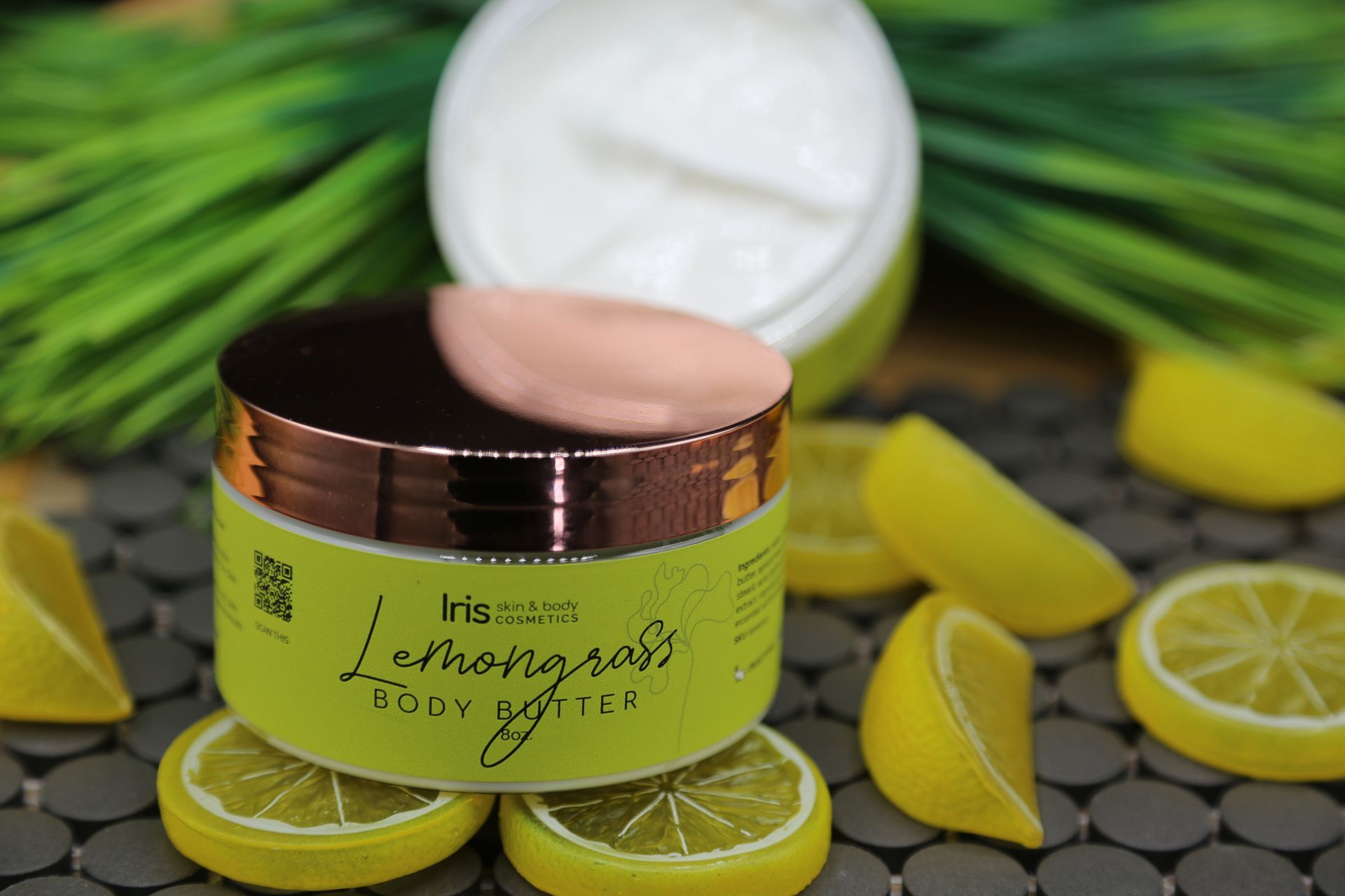 A jar of lemongrass body butter is surrounded by lemon slices.