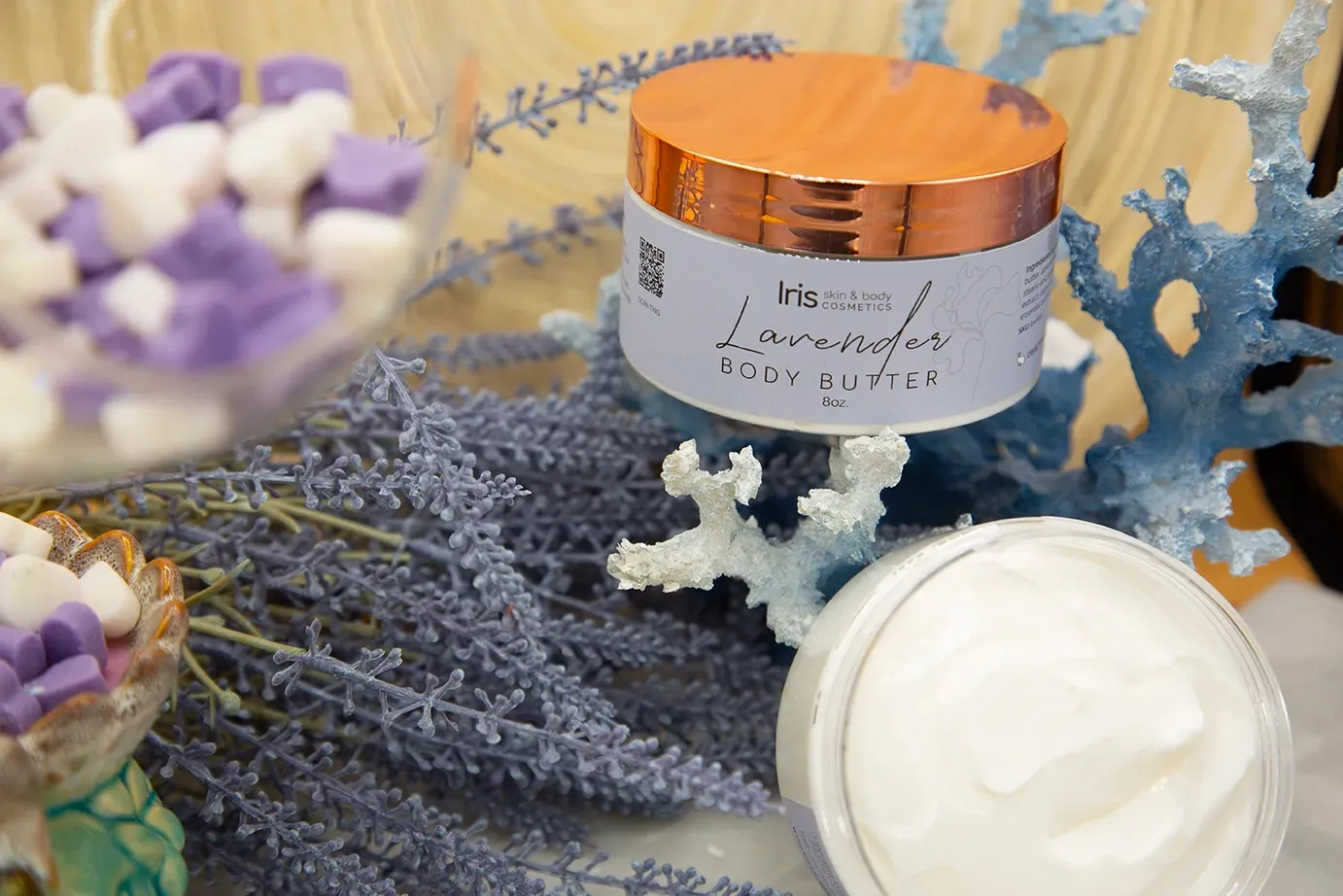 A jar of cream is sitting on a table next to flowers and coral.