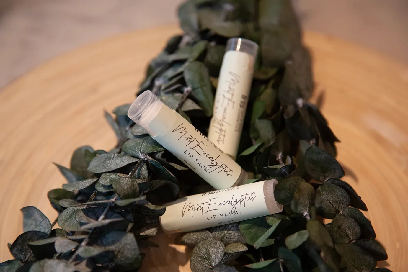 Three tubes of lip balm are sitting on top of a wooden table.