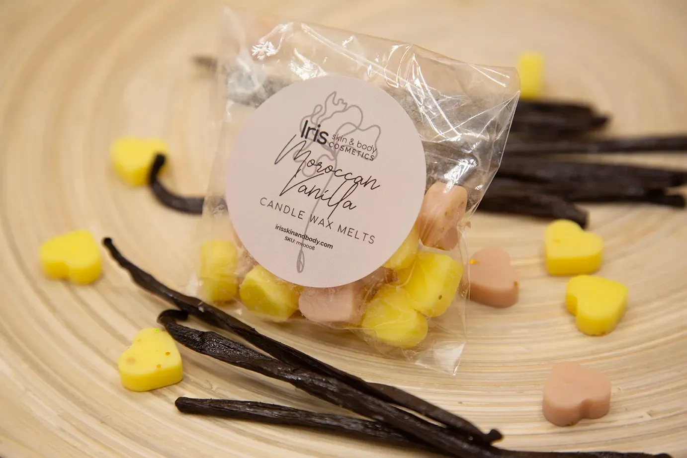 A bag of wax melts and vanilla sticks on a wooden table.