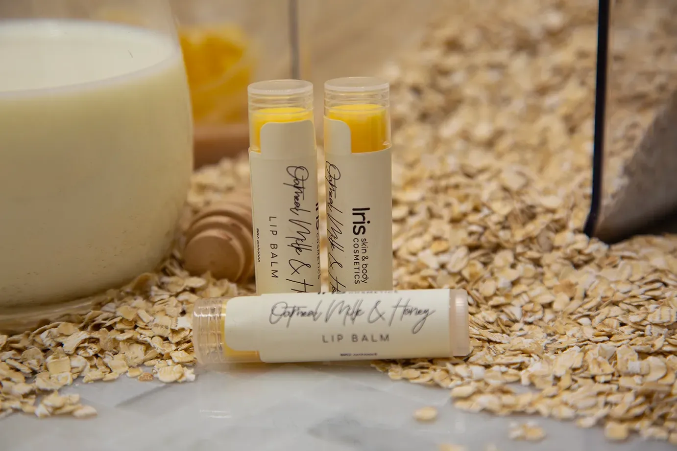 Three lip balms are sitting on top of a pile of oats next to a glass of milk.