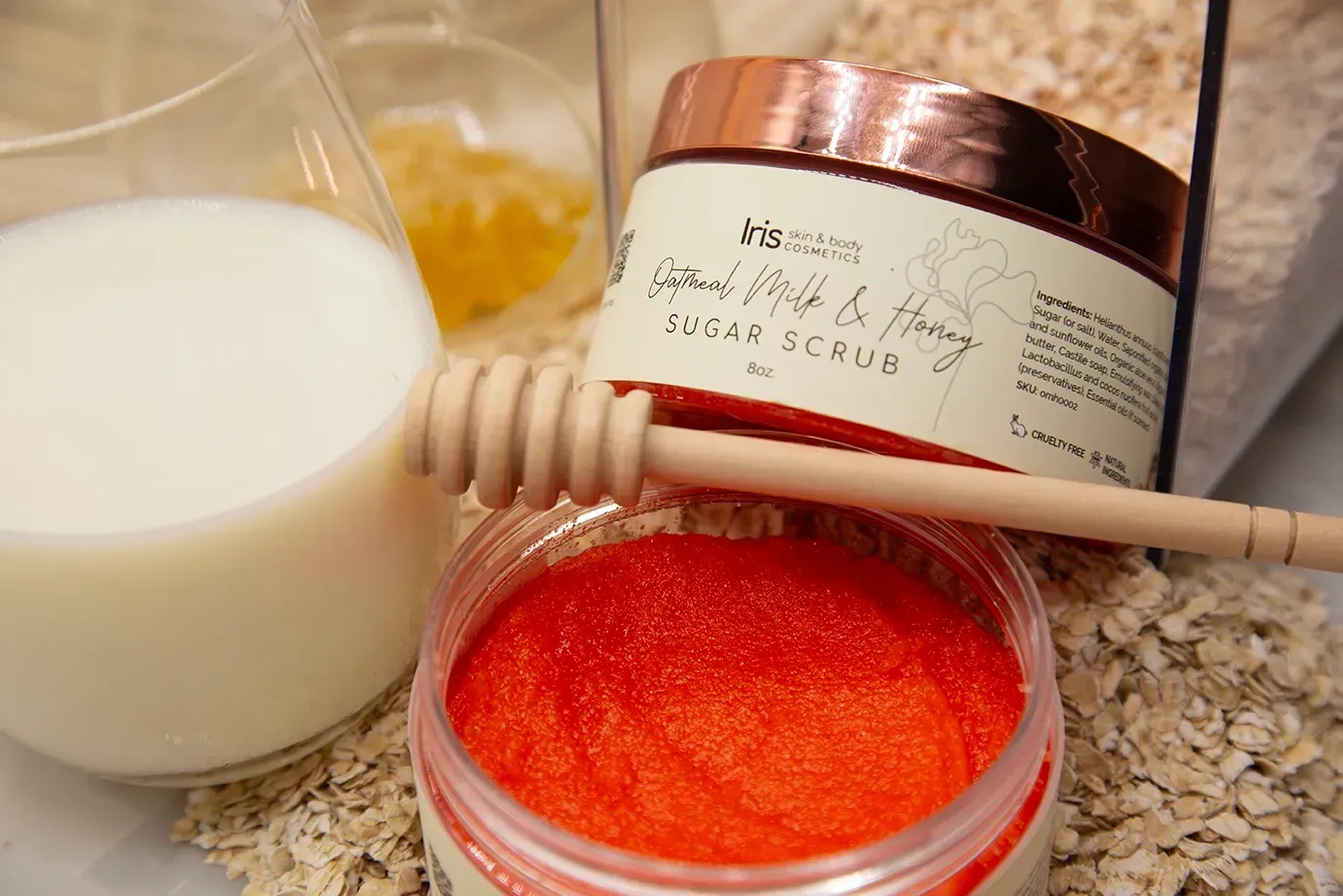 A jar of body scrub with a honey dipper next to a glass of milk.