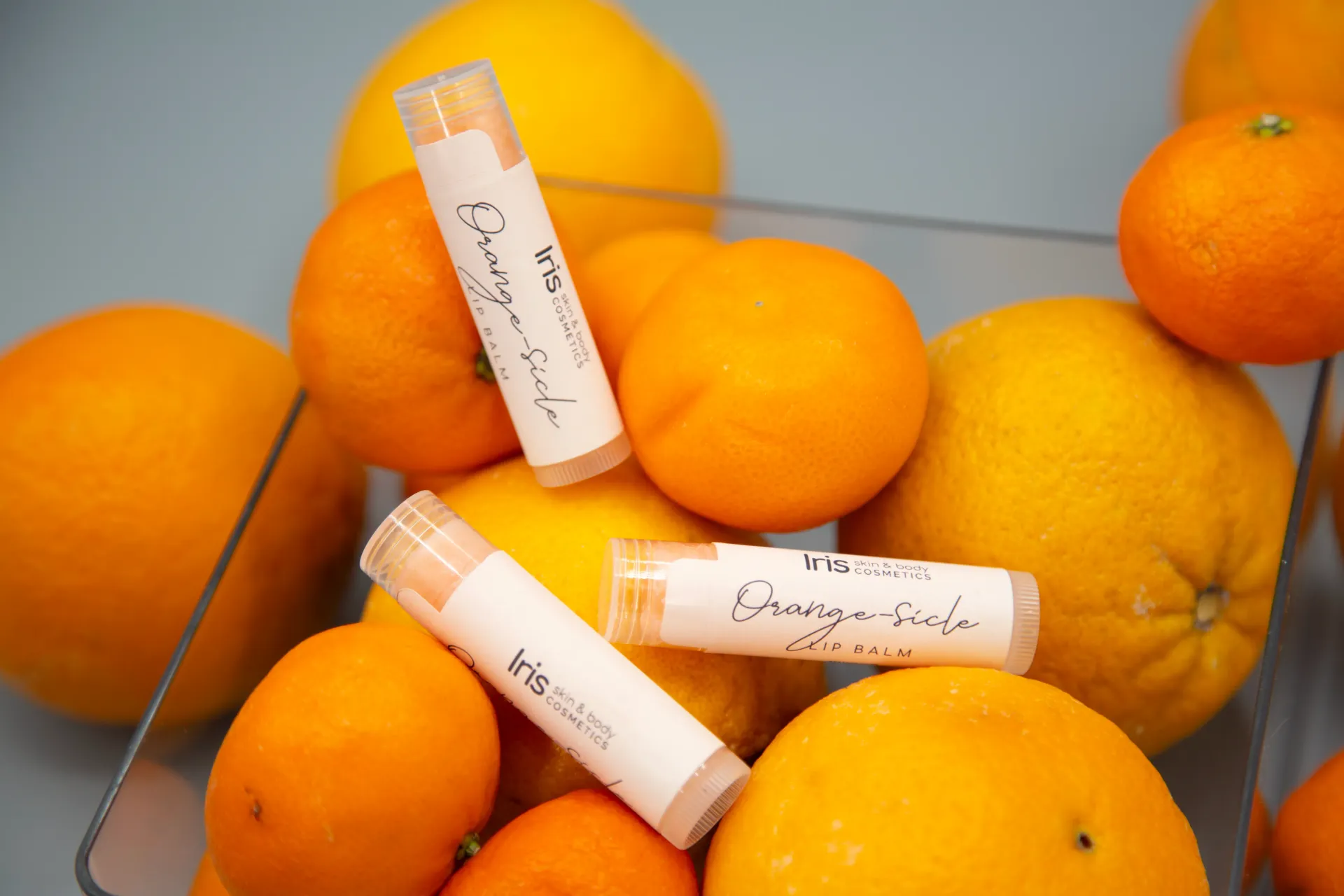 Three tubes of lip balm are sitting on top of a pile of oranges.
