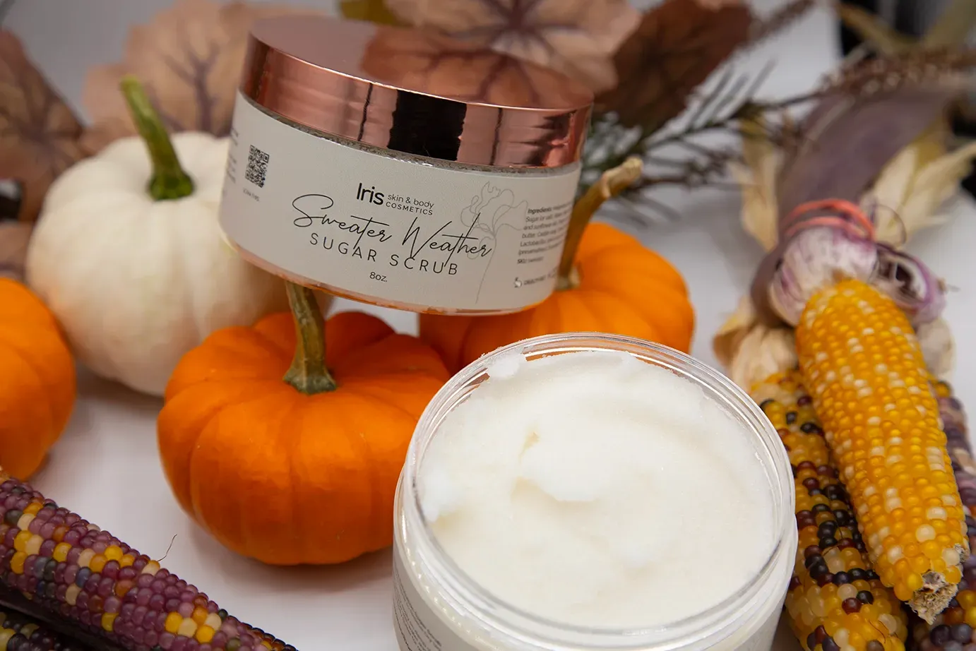 A jar of cream is sitting on a table next to pumpkins and corn on the cob.