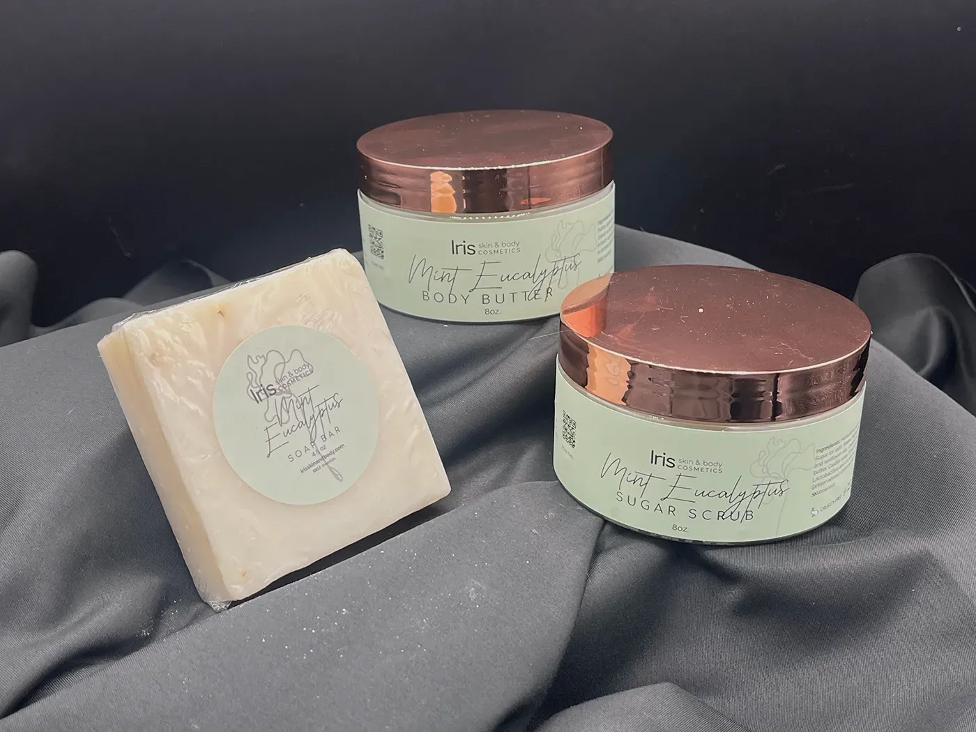A soap and two jars of cream are sitting on a cloth.