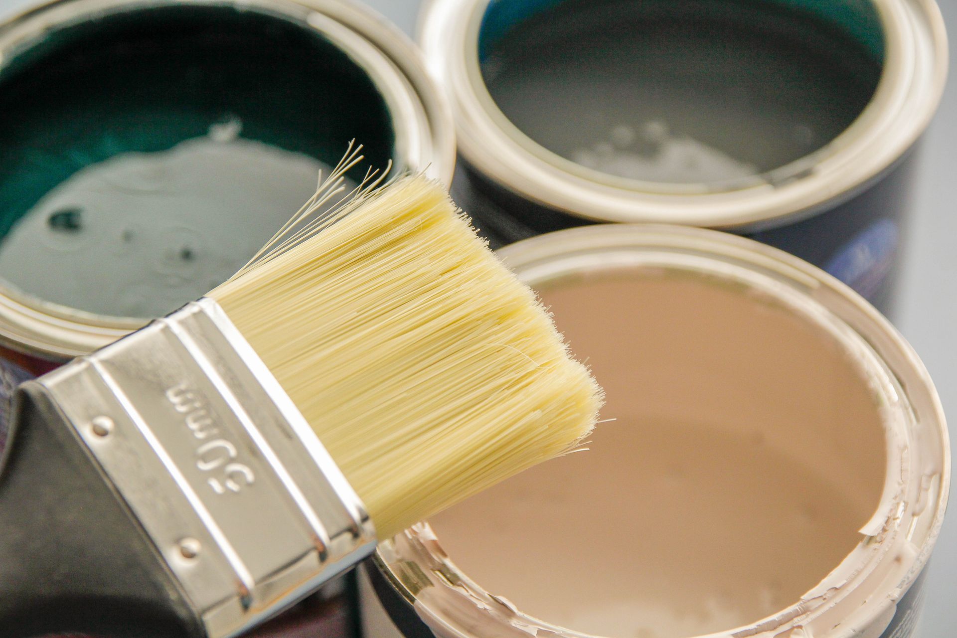 Three open paint cans with dark green, blue, and beige colors; brush above.