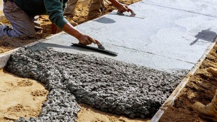 A man is spreading concrete on a sidewalk with a trowel.