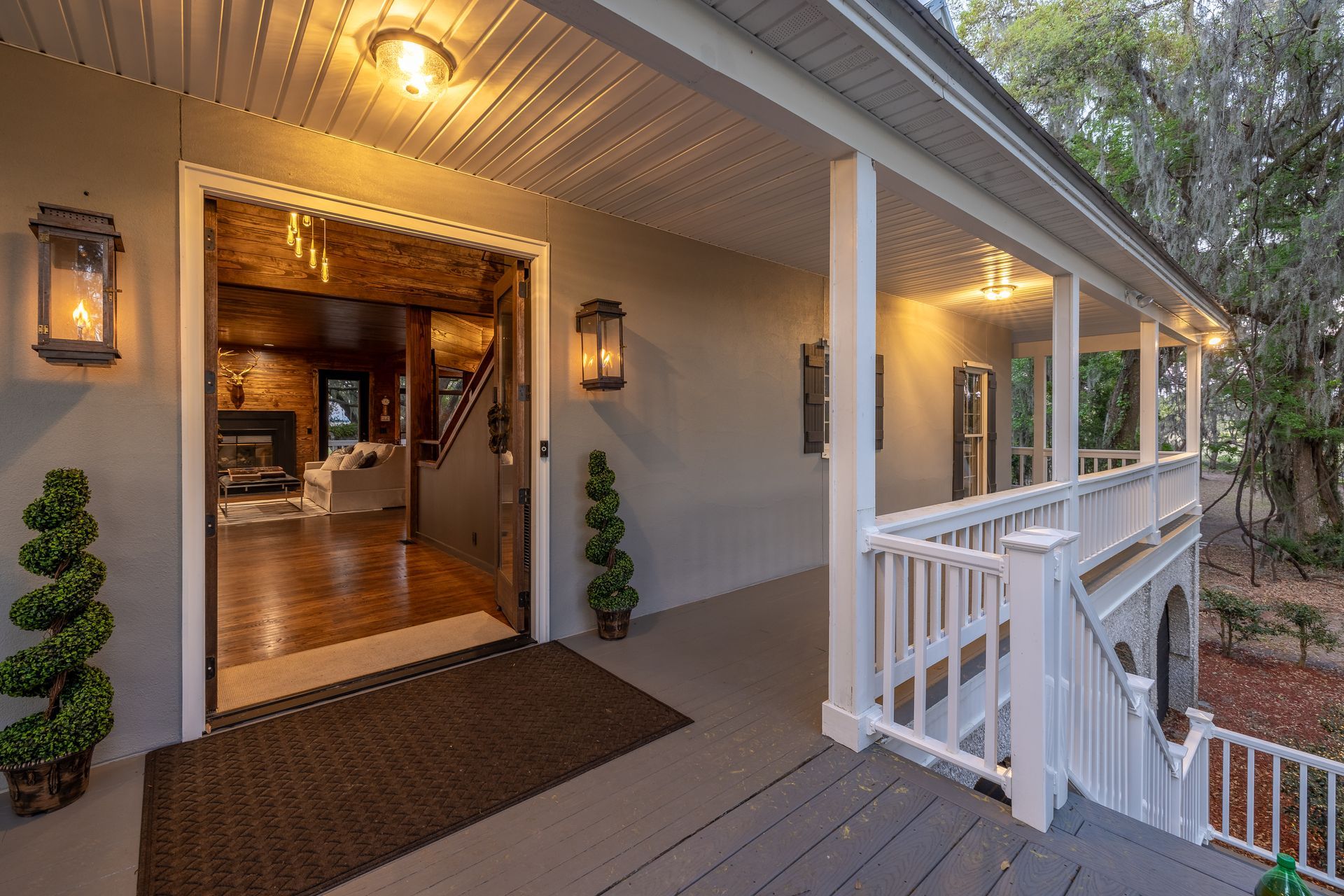 Front porch of a house with open doorway, showing living room with fireplace; gray siding, white trim.