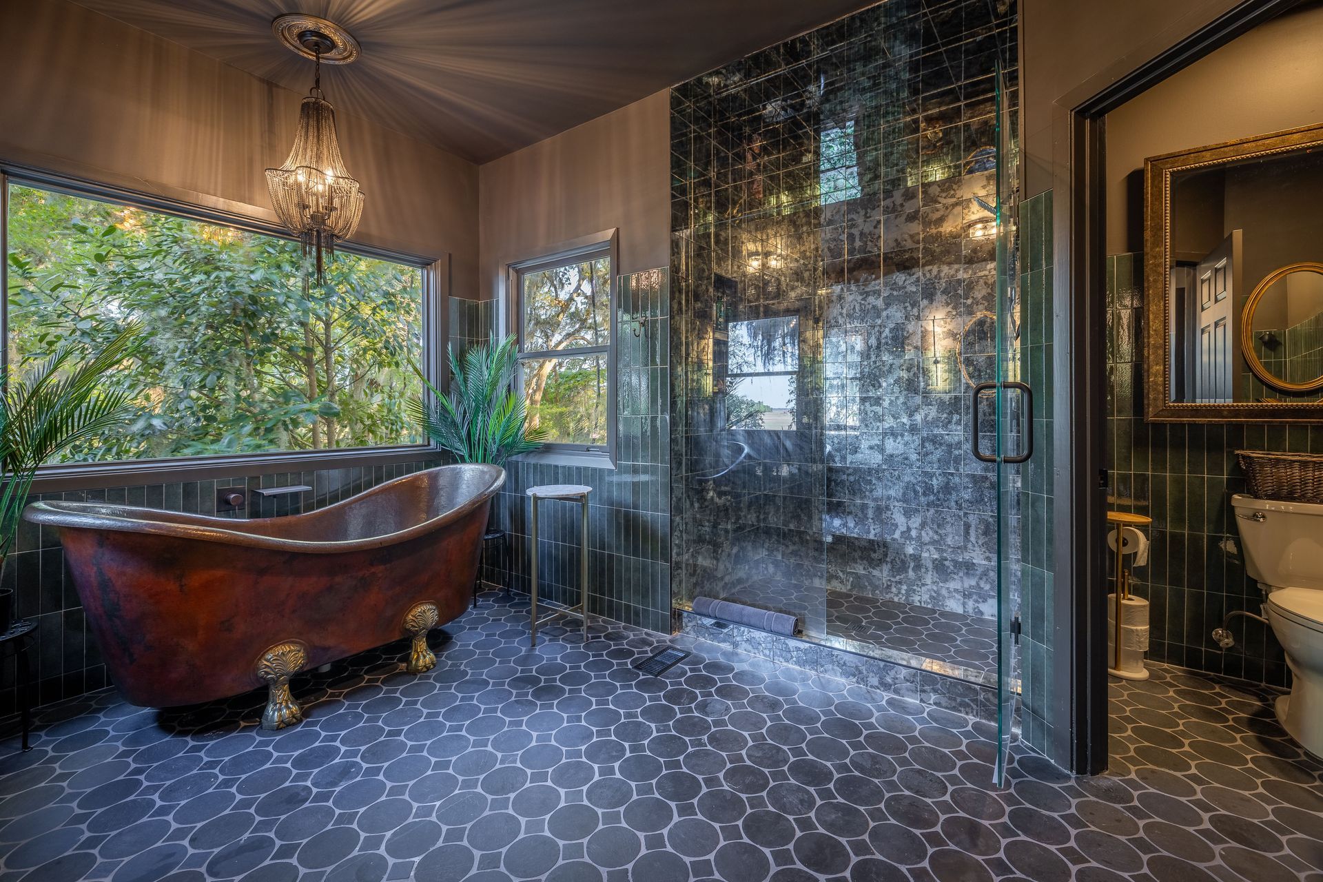 Luxurious bathroom with clawfoot tub, dark tiling, and large window overlooking greenery.