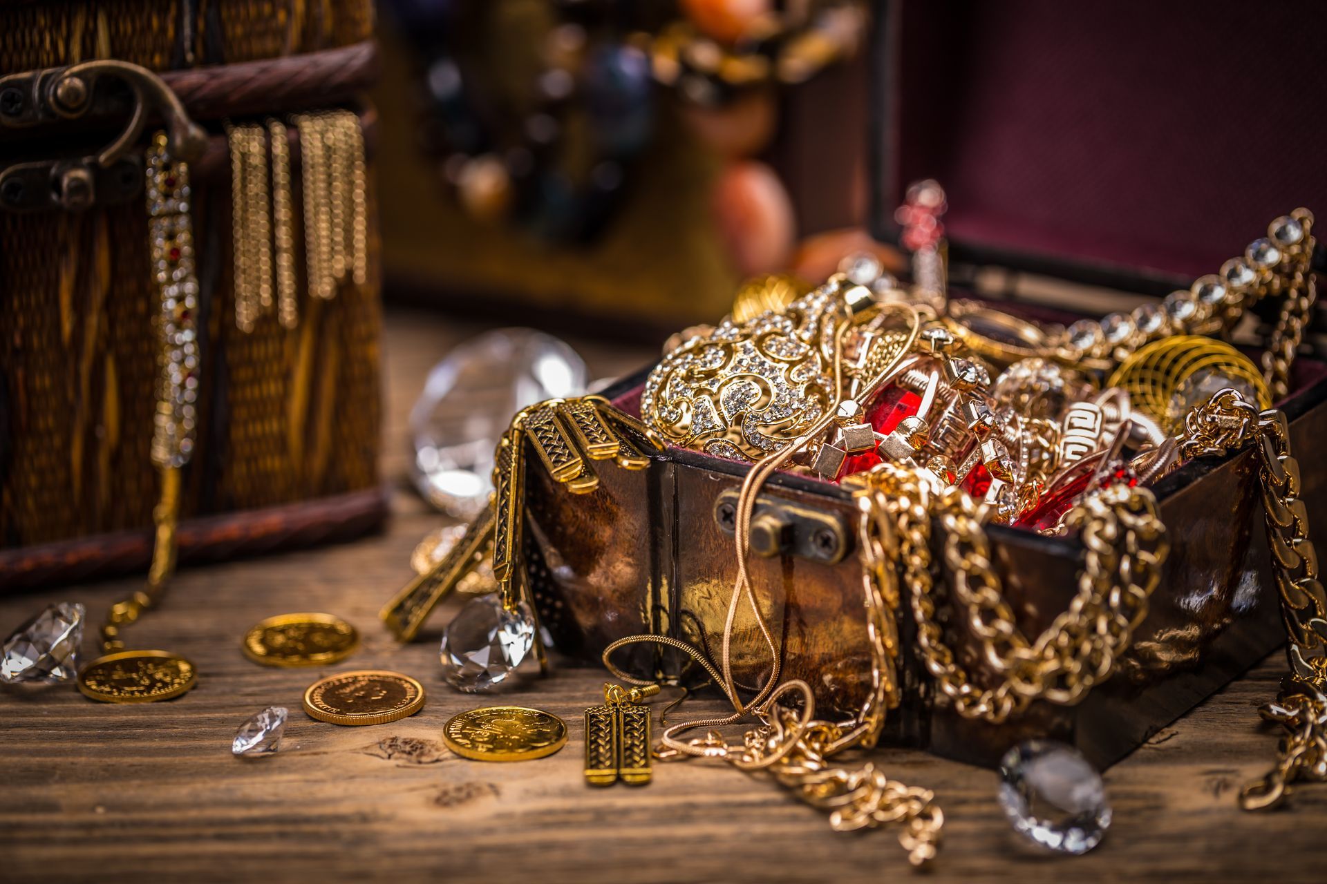 Treasure chests filled with gold jewelry, gems, and coins spilling onto a wooden surface.