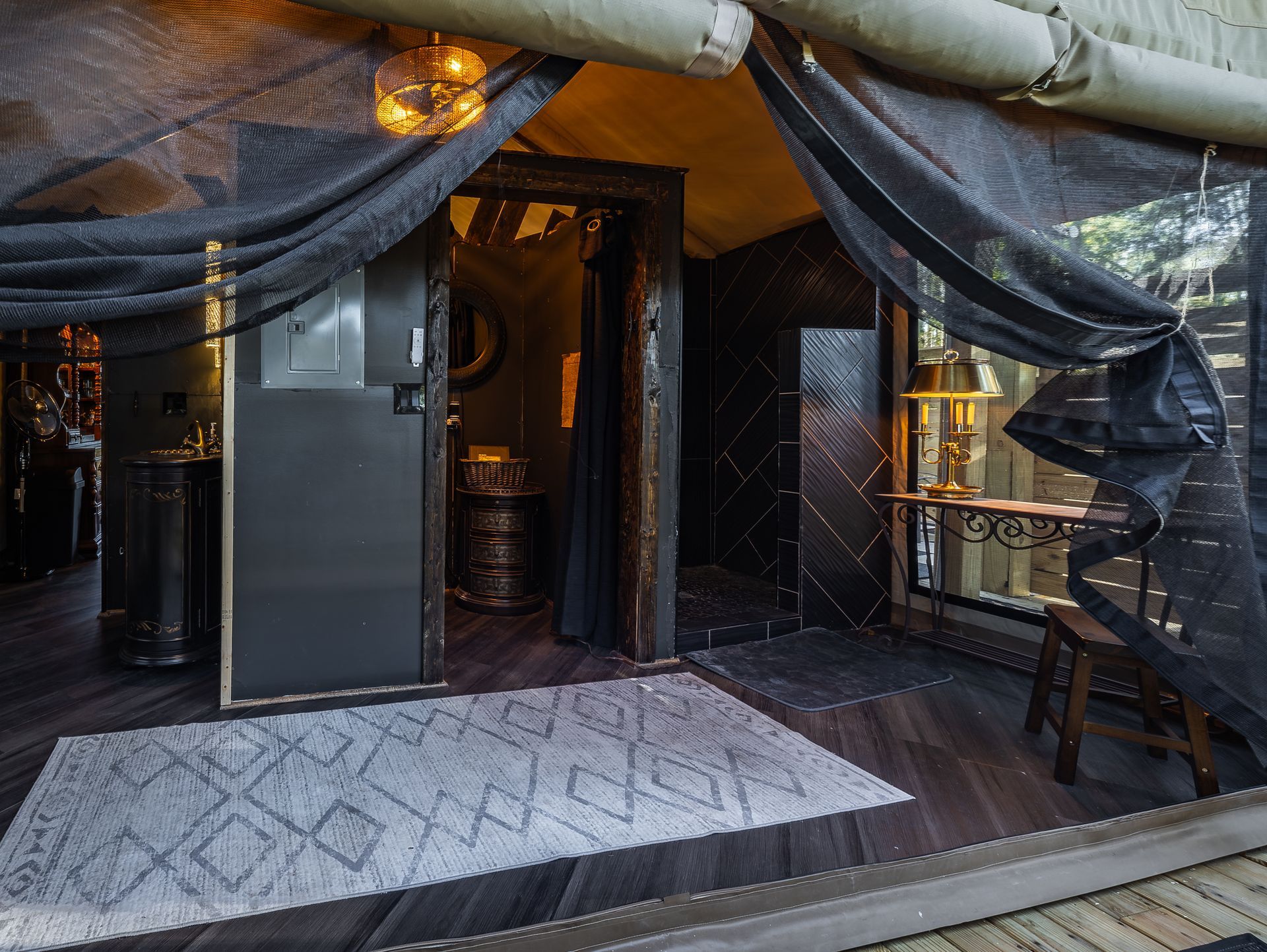 Dark glamping tent entrance with black draped fabric, gray rug, and interior fixtures visible.