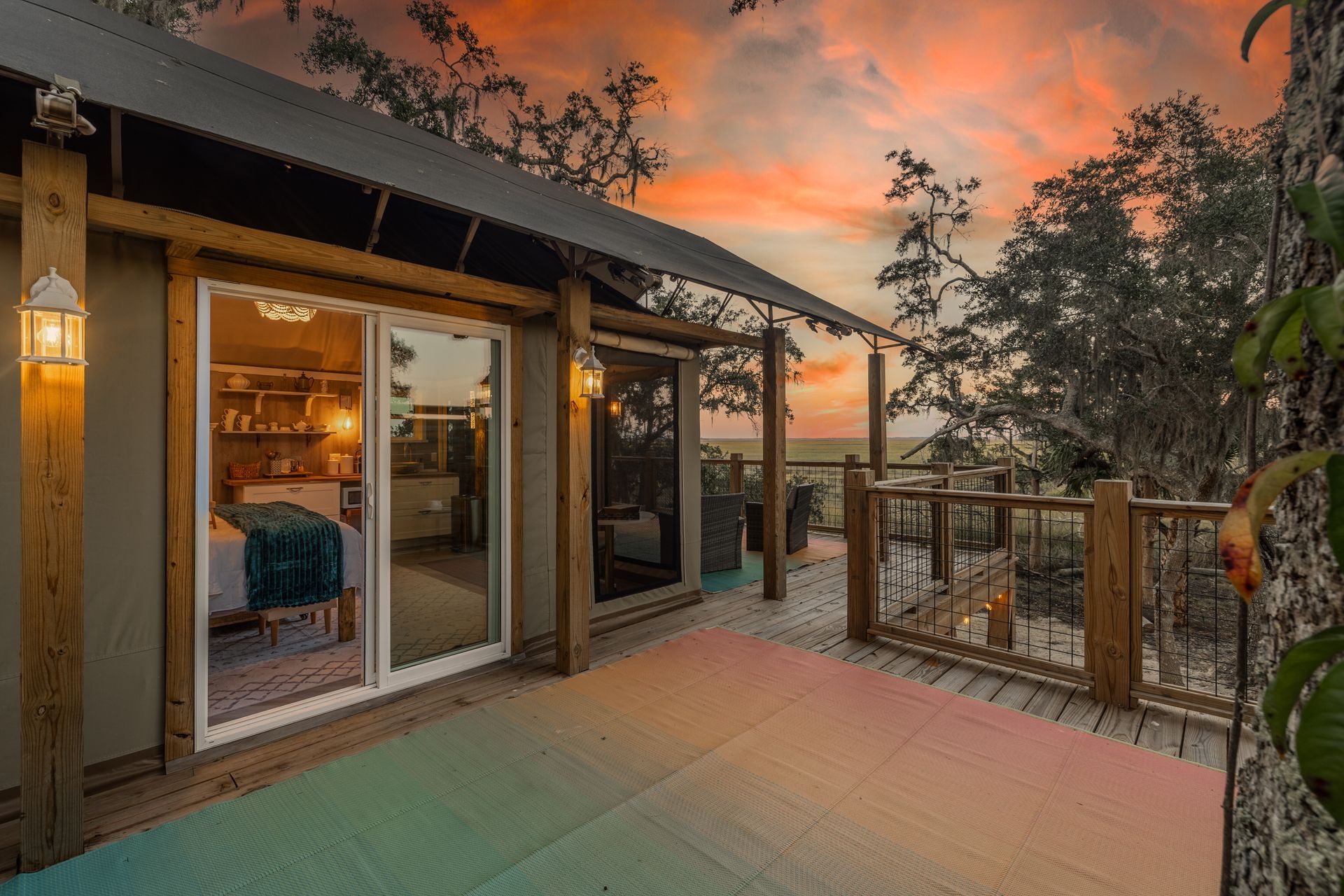 Cabin with deck overlooking a sunset. Wooden structure with glass sliding doors, outdoor seating, and colorful patio.