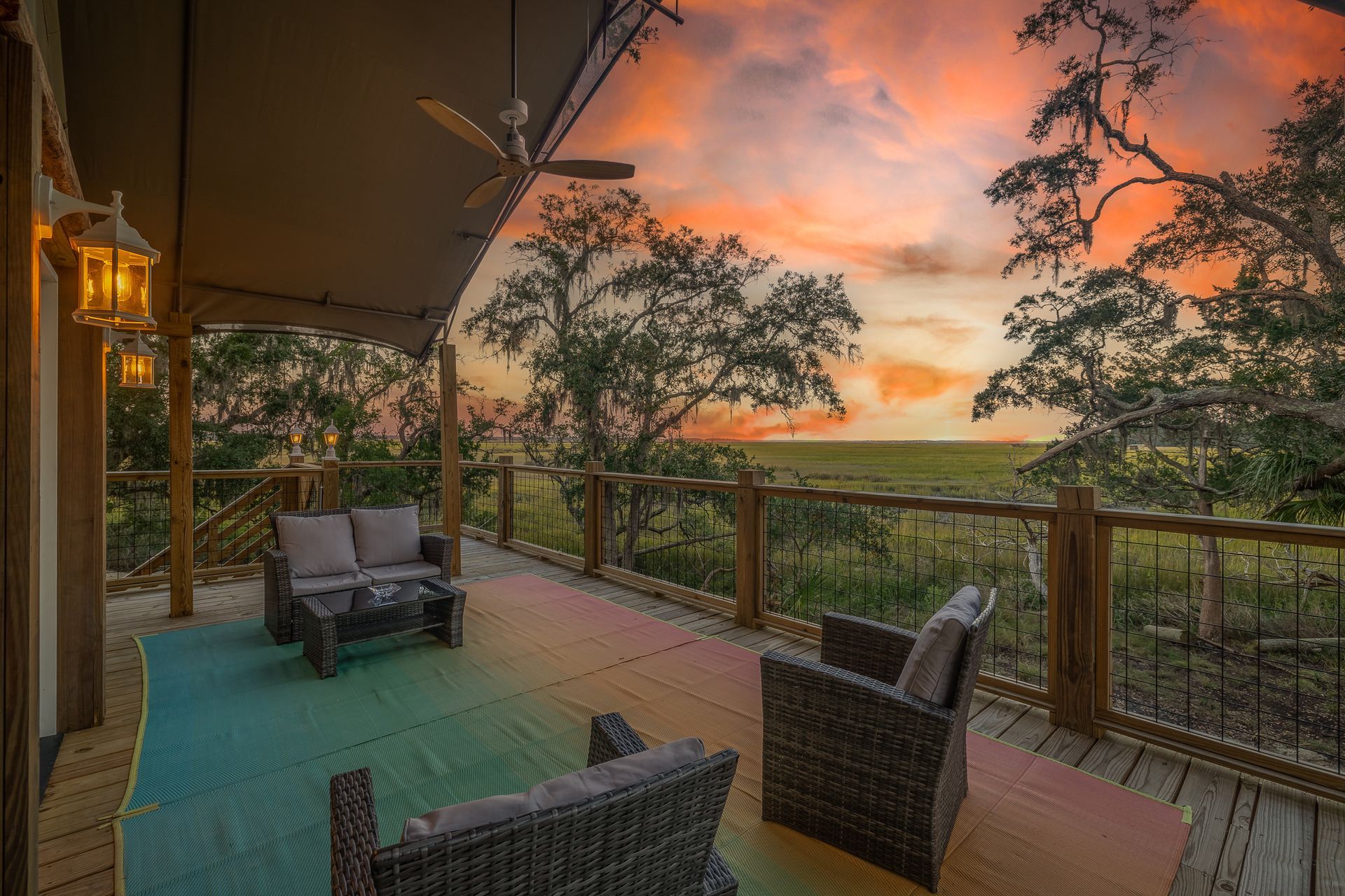 Patio with wicker furniture, colorful rug, and sunset view from a glamping tent.