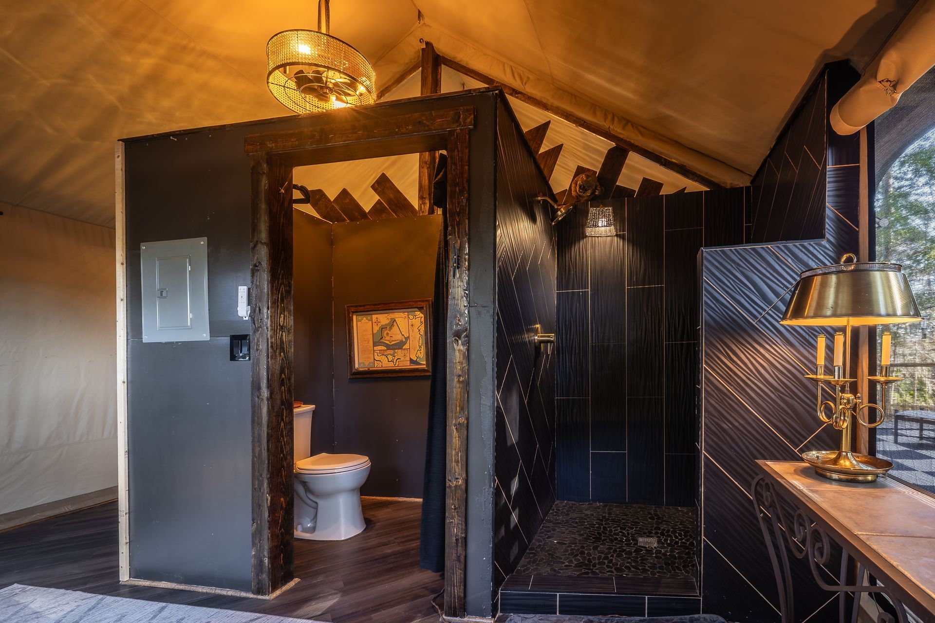 Interior of a luxury bathroom with a toilet and shower in a tent structure, dark decor, gold accents.