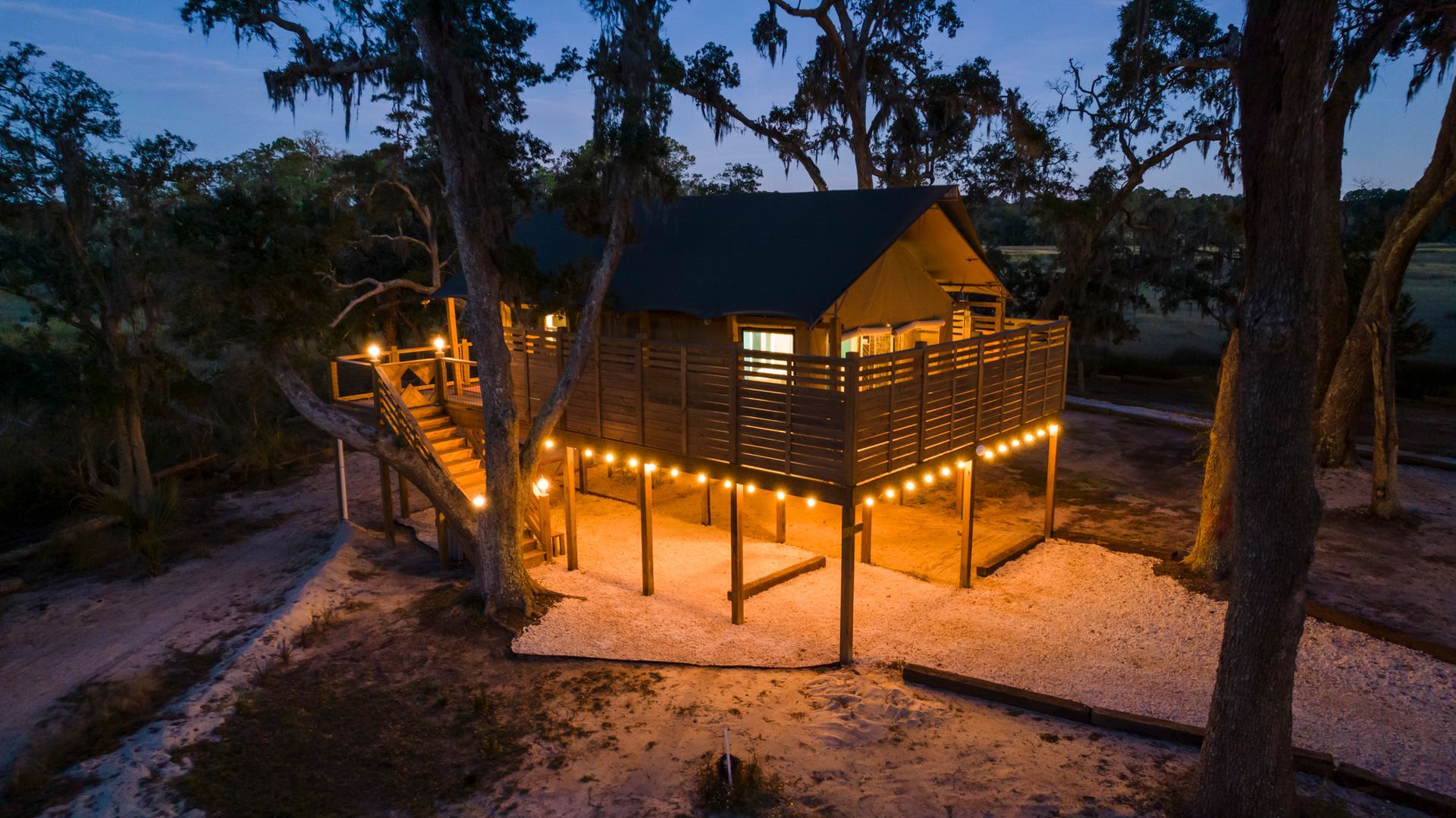 Wooden cabin lit with string lights at dusk, surrounded by trees.