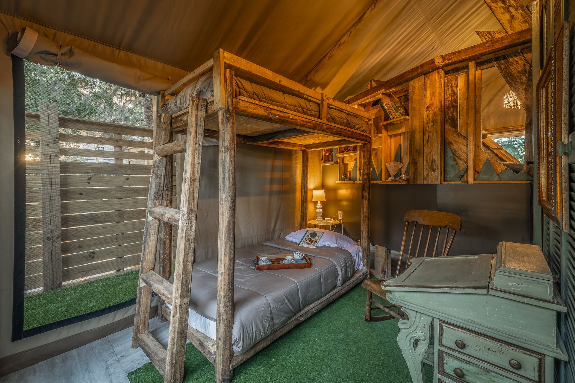 Rustic tent interior with wooden bunk bed, small desk, and lawn-like floor.