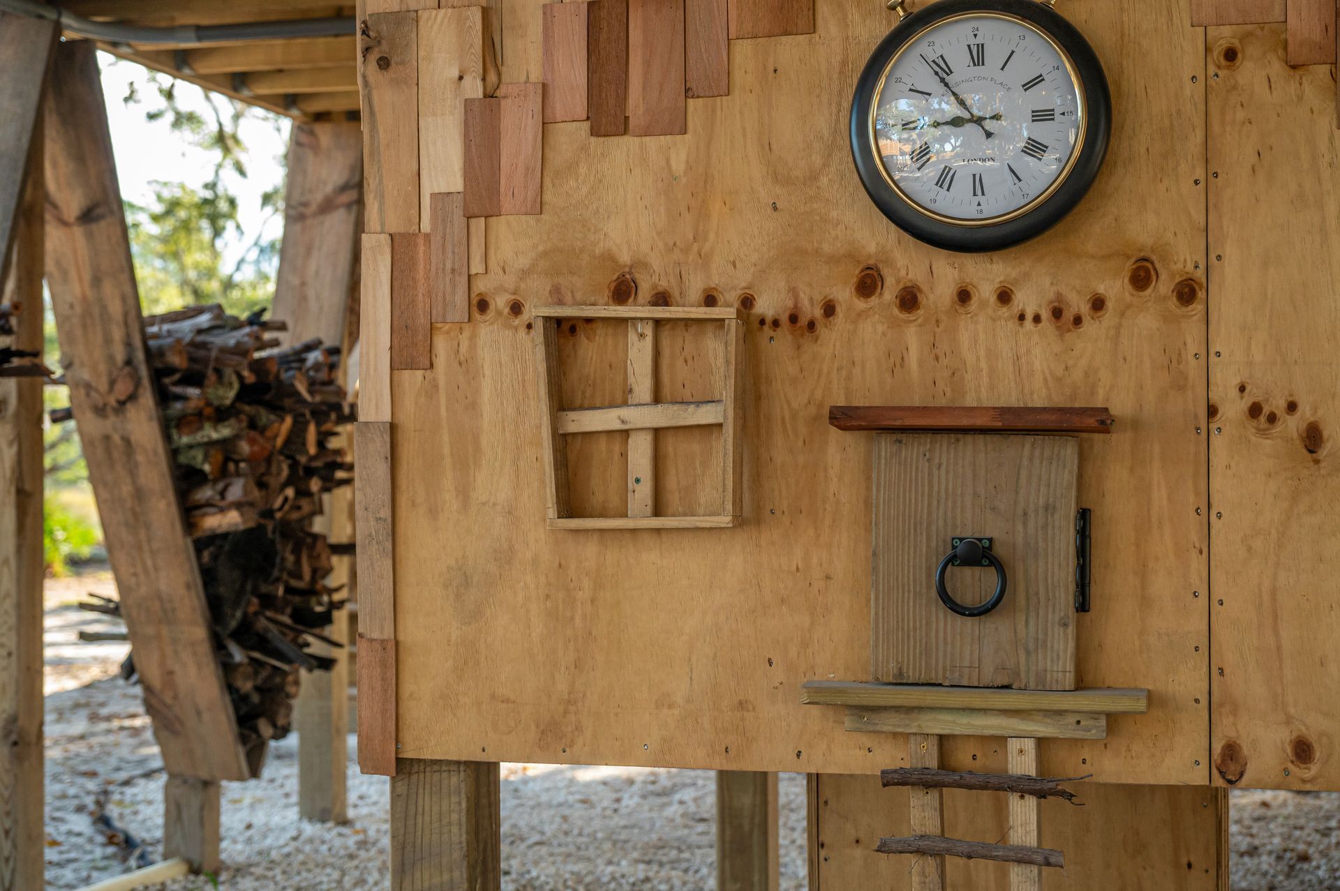 Wooden structure with clock, small door, window, and woodpile.
