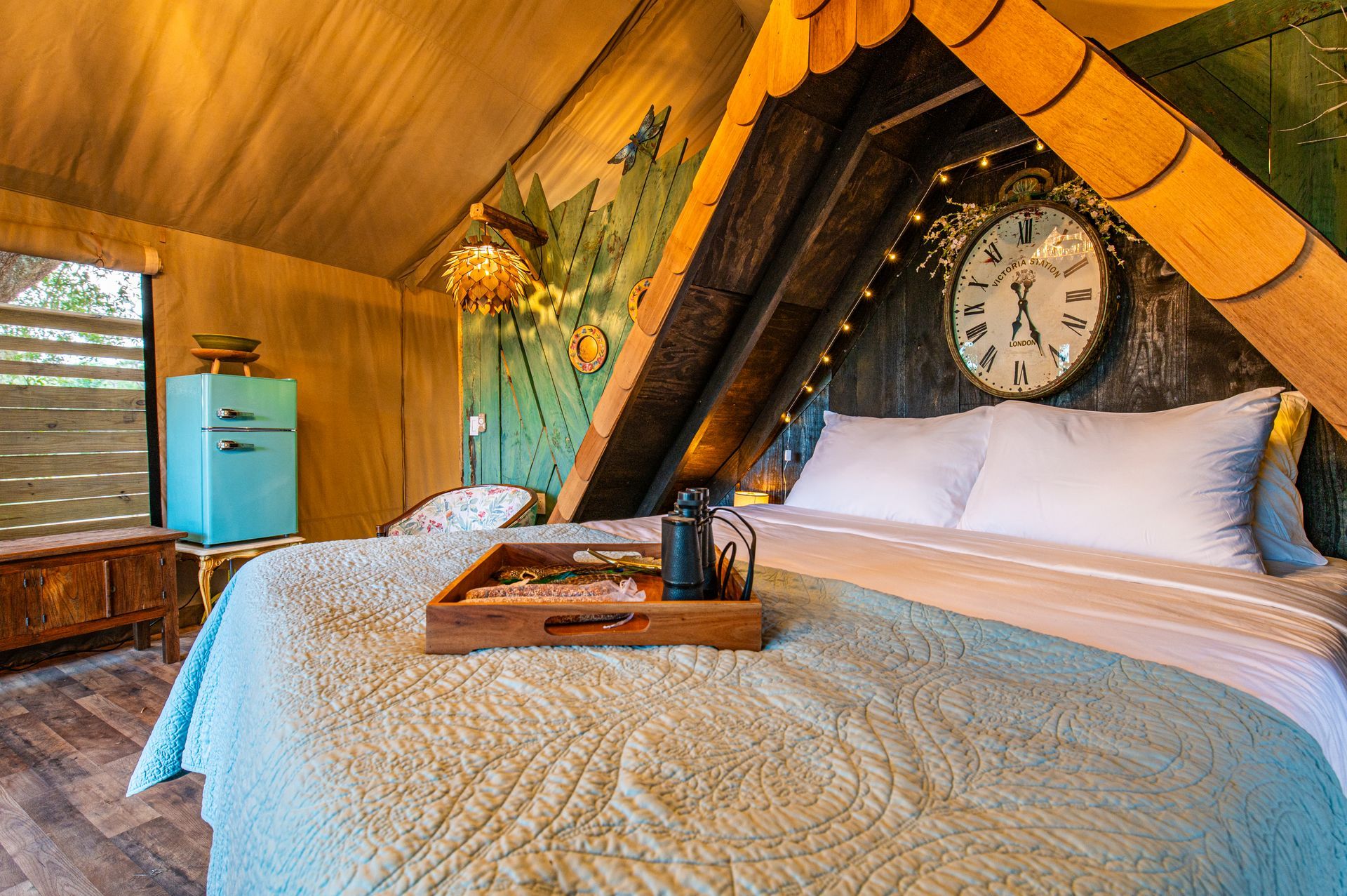 Cozy glamping tent interior with bed, clock, fridge, and wooden accents.