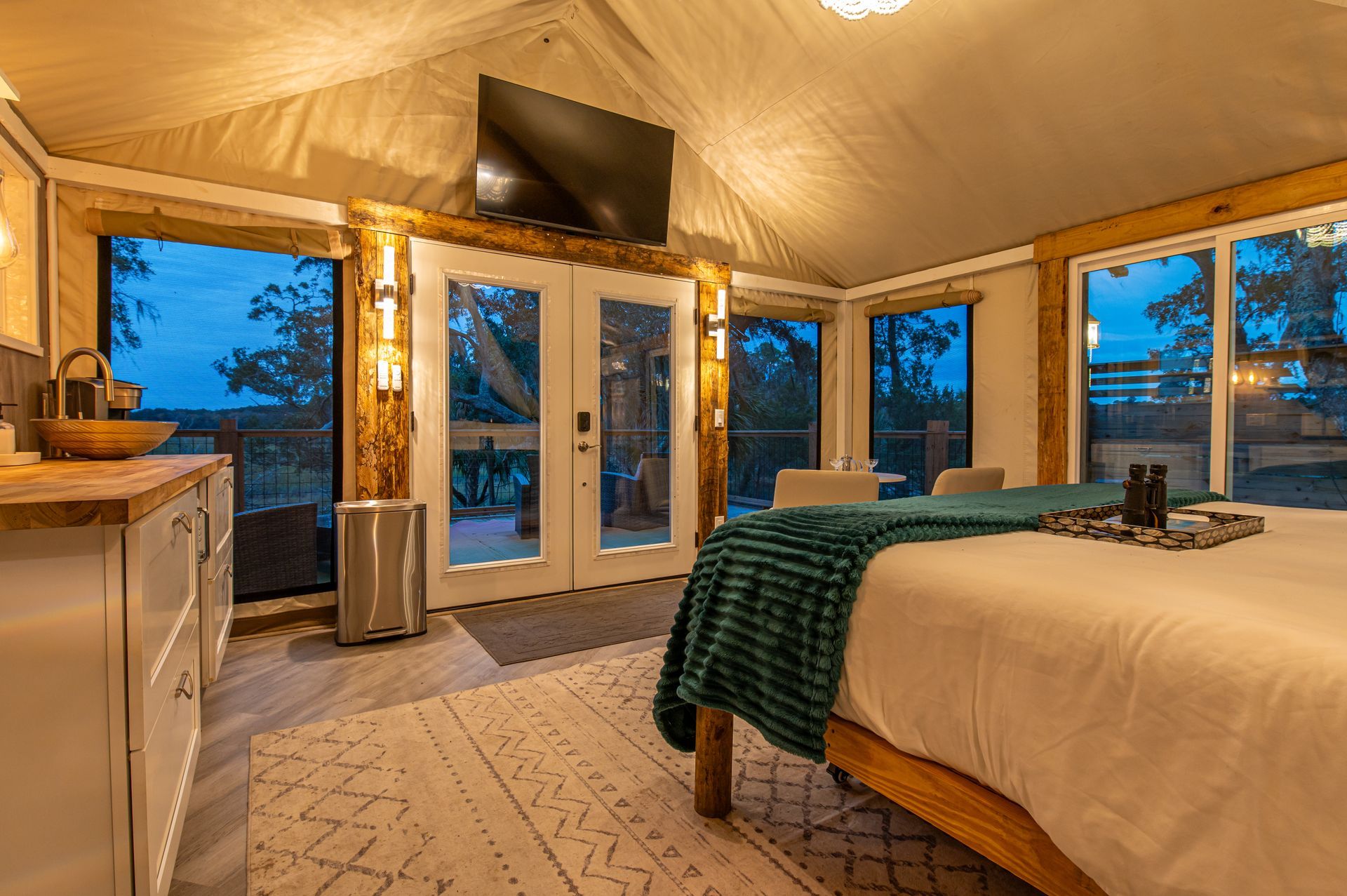 Glamping tent interior with bed, TV, and windows overlooking the outdoors.