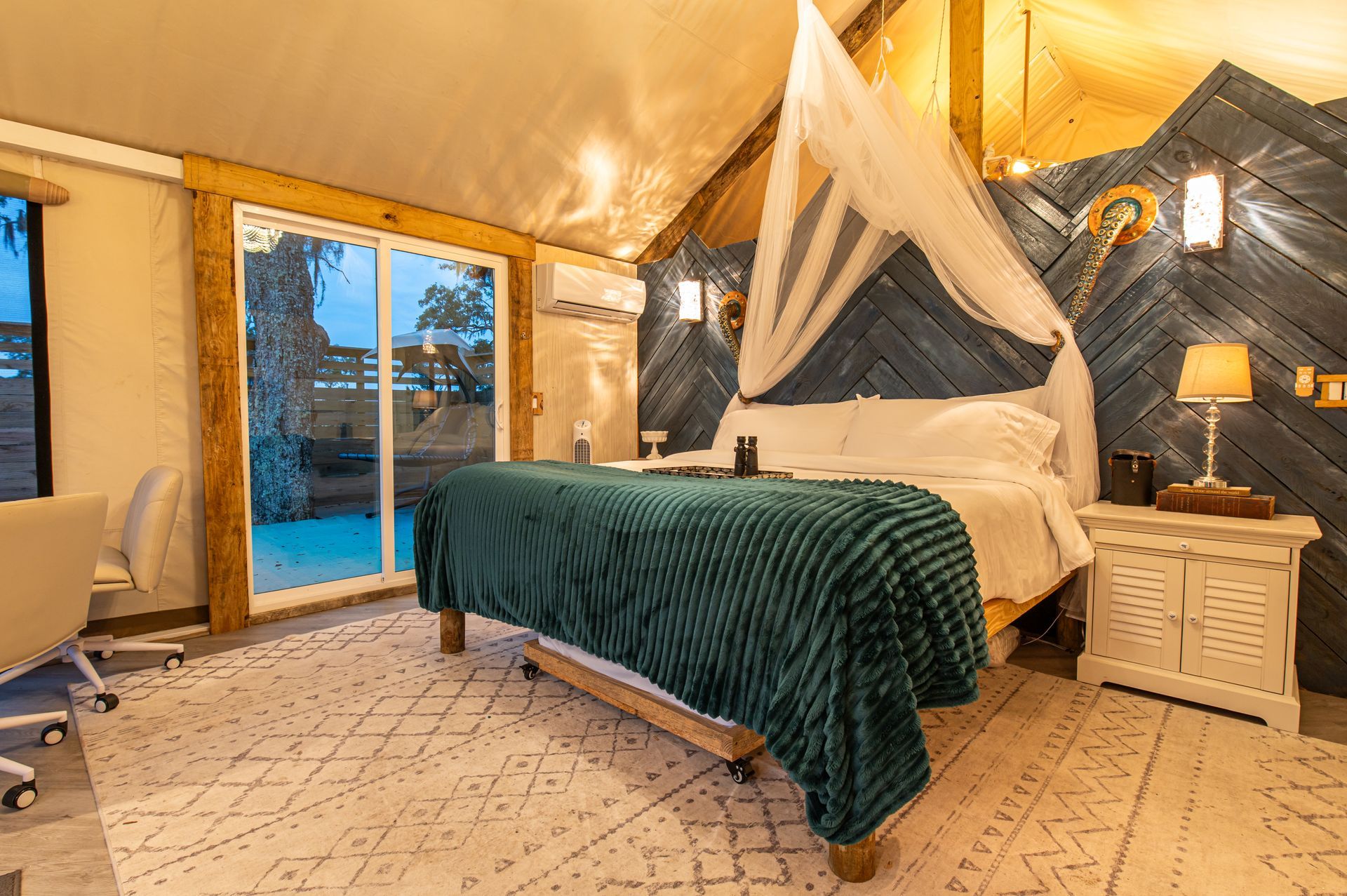 Glamping tent interior with bed, sliding glass door, and a desk.