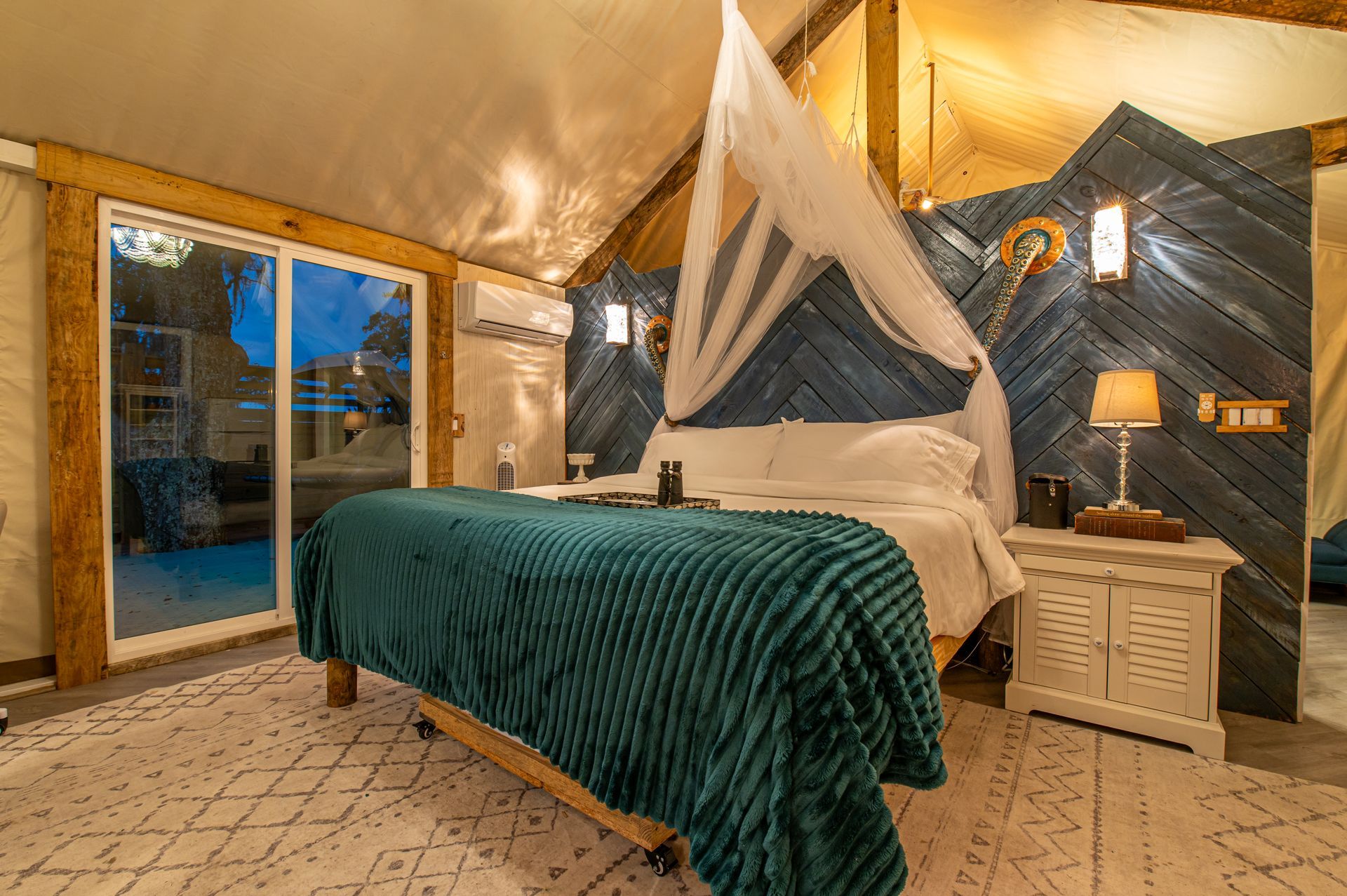 Bedroom with a bed, teal blanket, white rug, sliding door, and decorative wall.