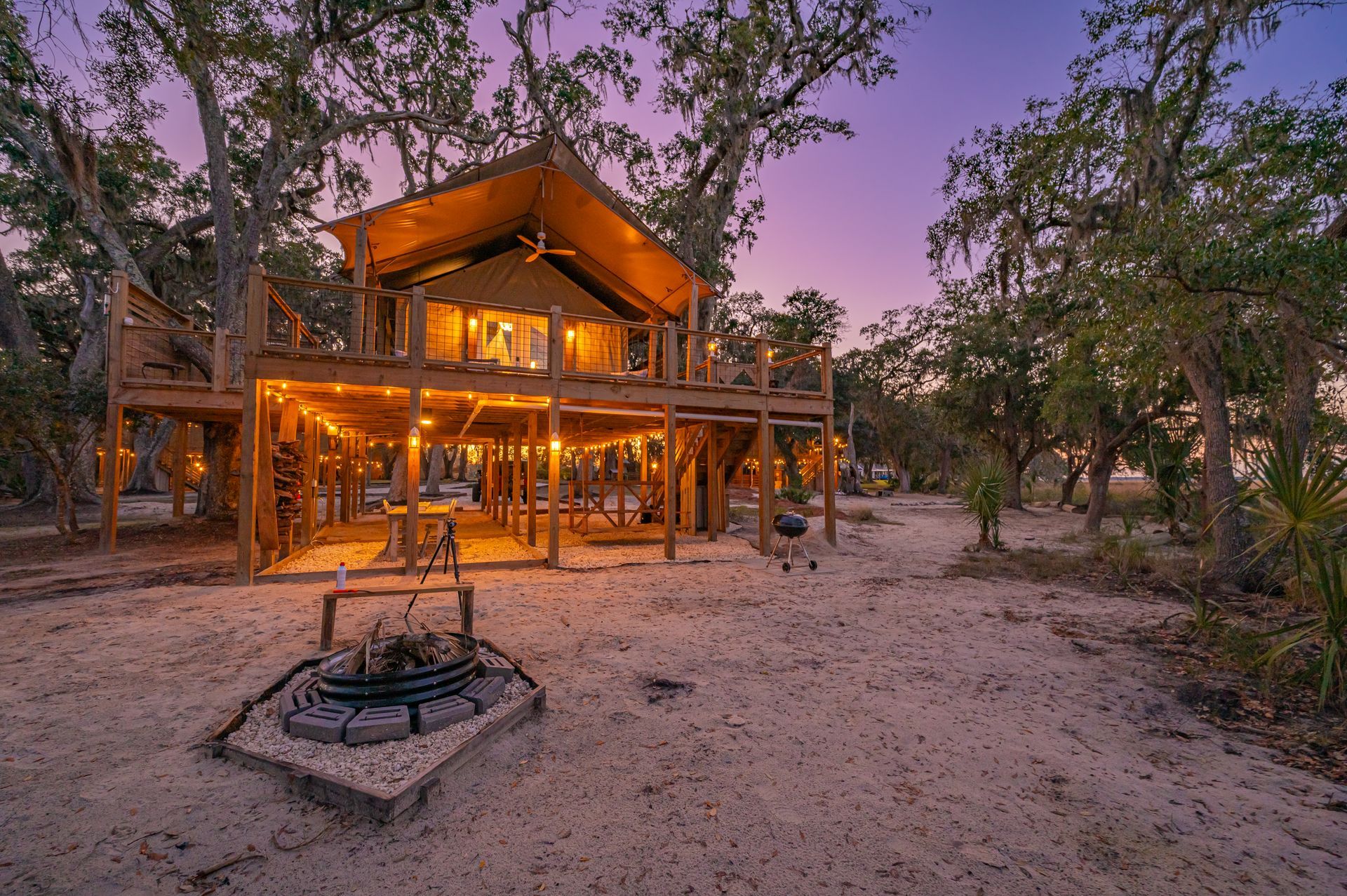 Treehouse glamping setup at dusk with string lights and fire pit.