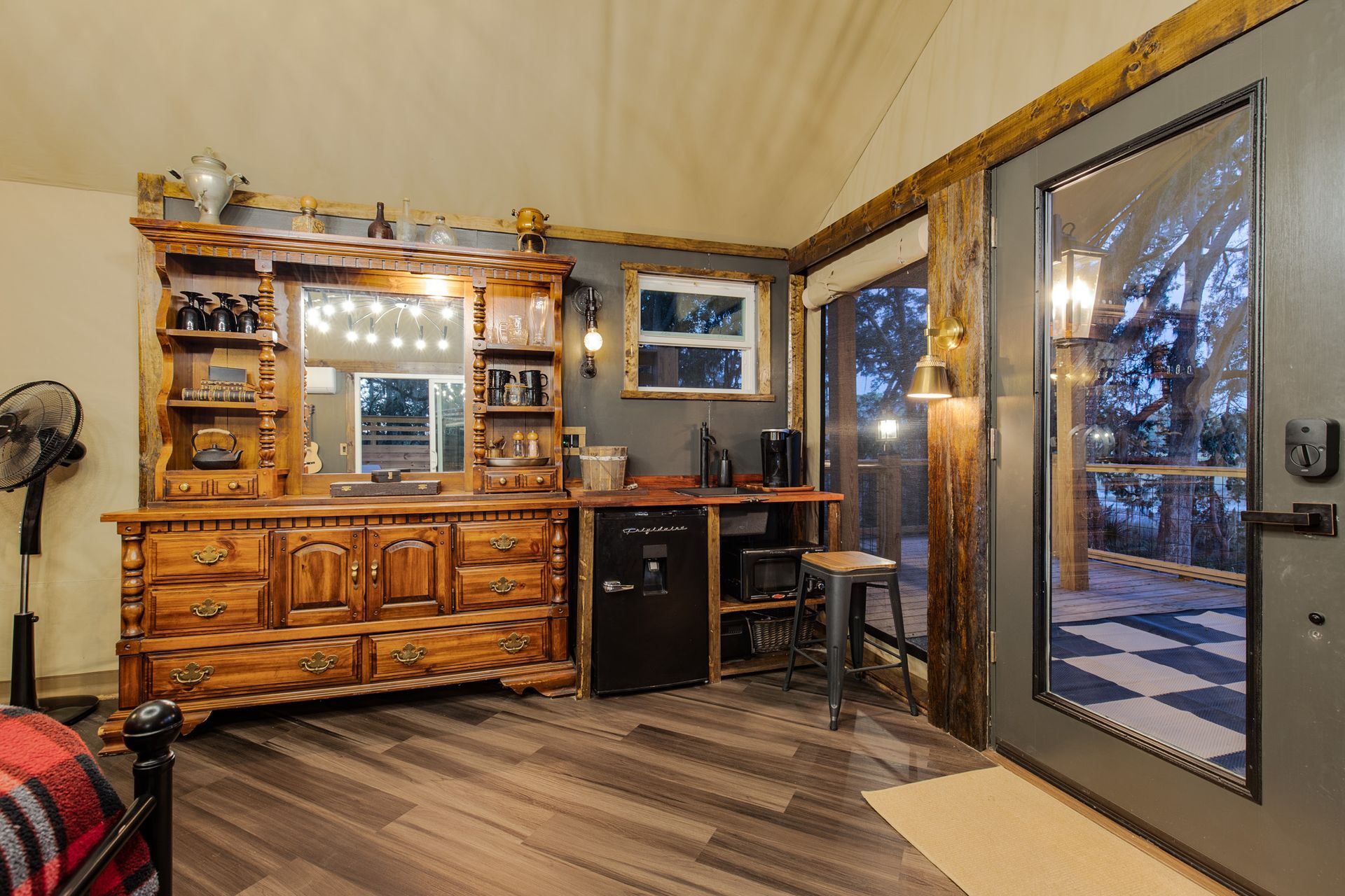 Rustic cabin interior with wooden dresser, mini-fridge, and door to a deck.