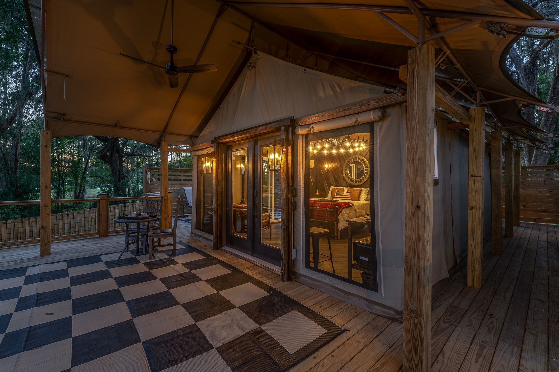Glamping tent with a checkerboard patio and lit interior visible through glass doors.