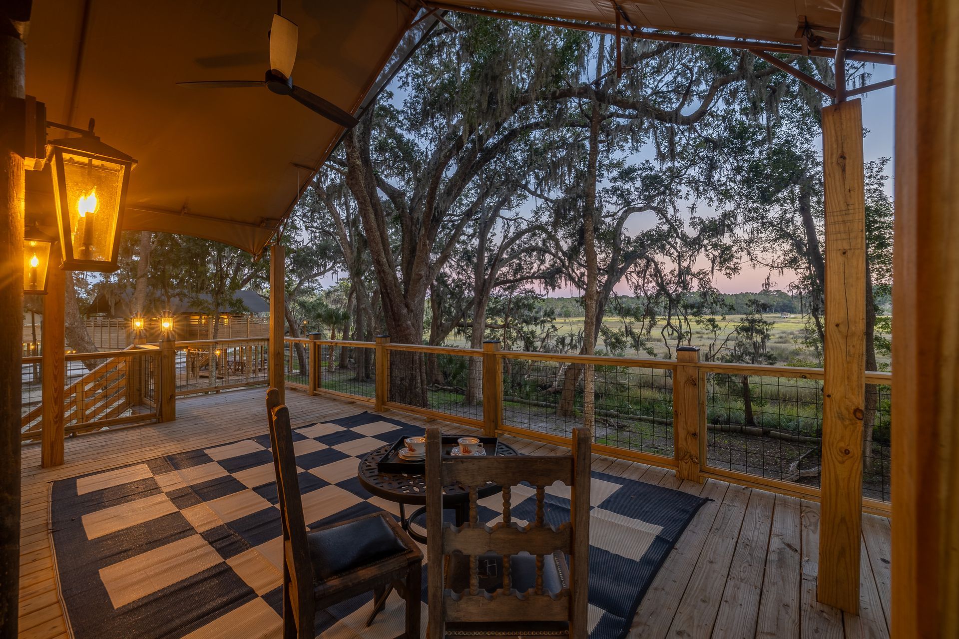 Outdoor porch of a glamping tent with a wooden deck, rug, chairs, and view of a field.