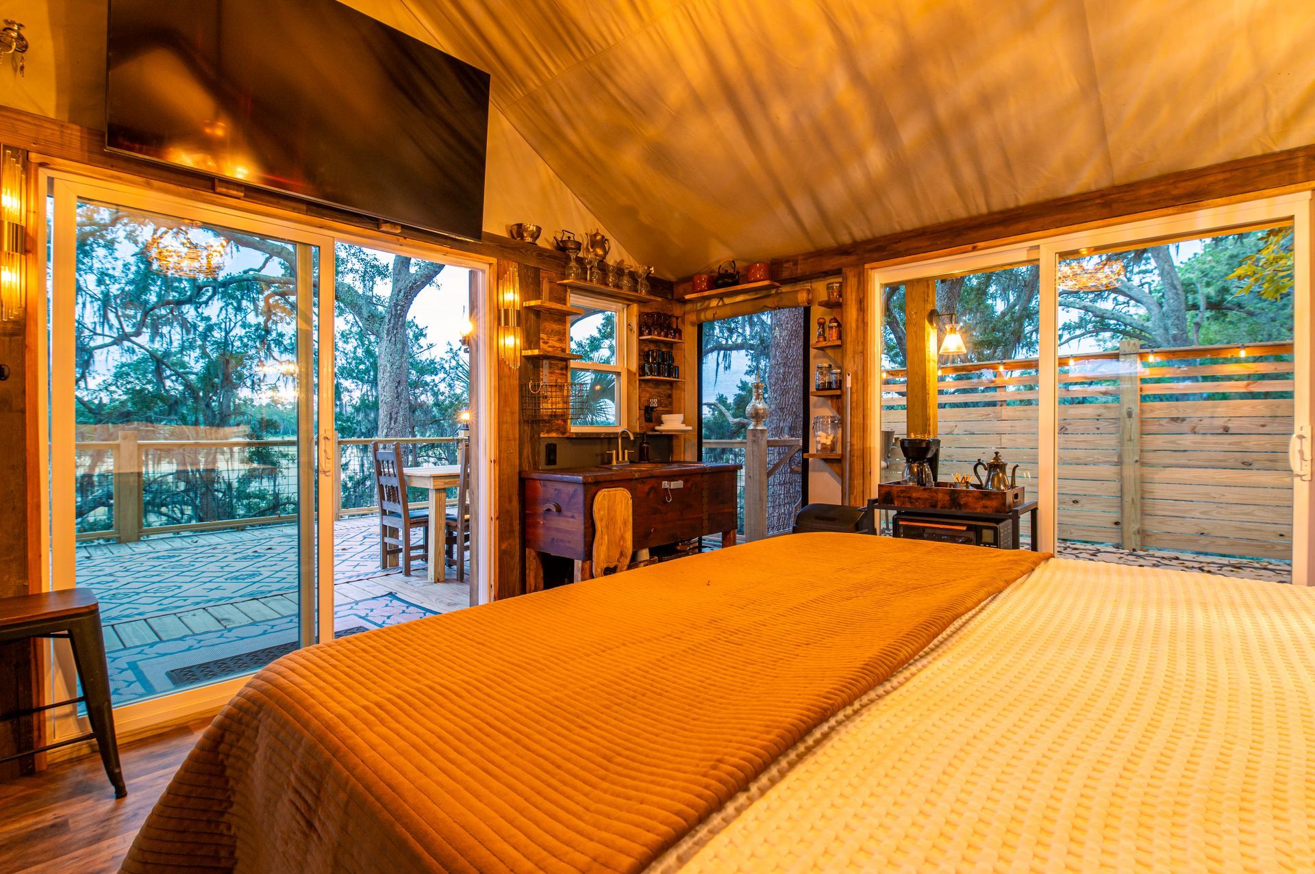 Cozy bedroom with sliding glass doors opening to a deck. Orange blanket on the bed, warm lighting.