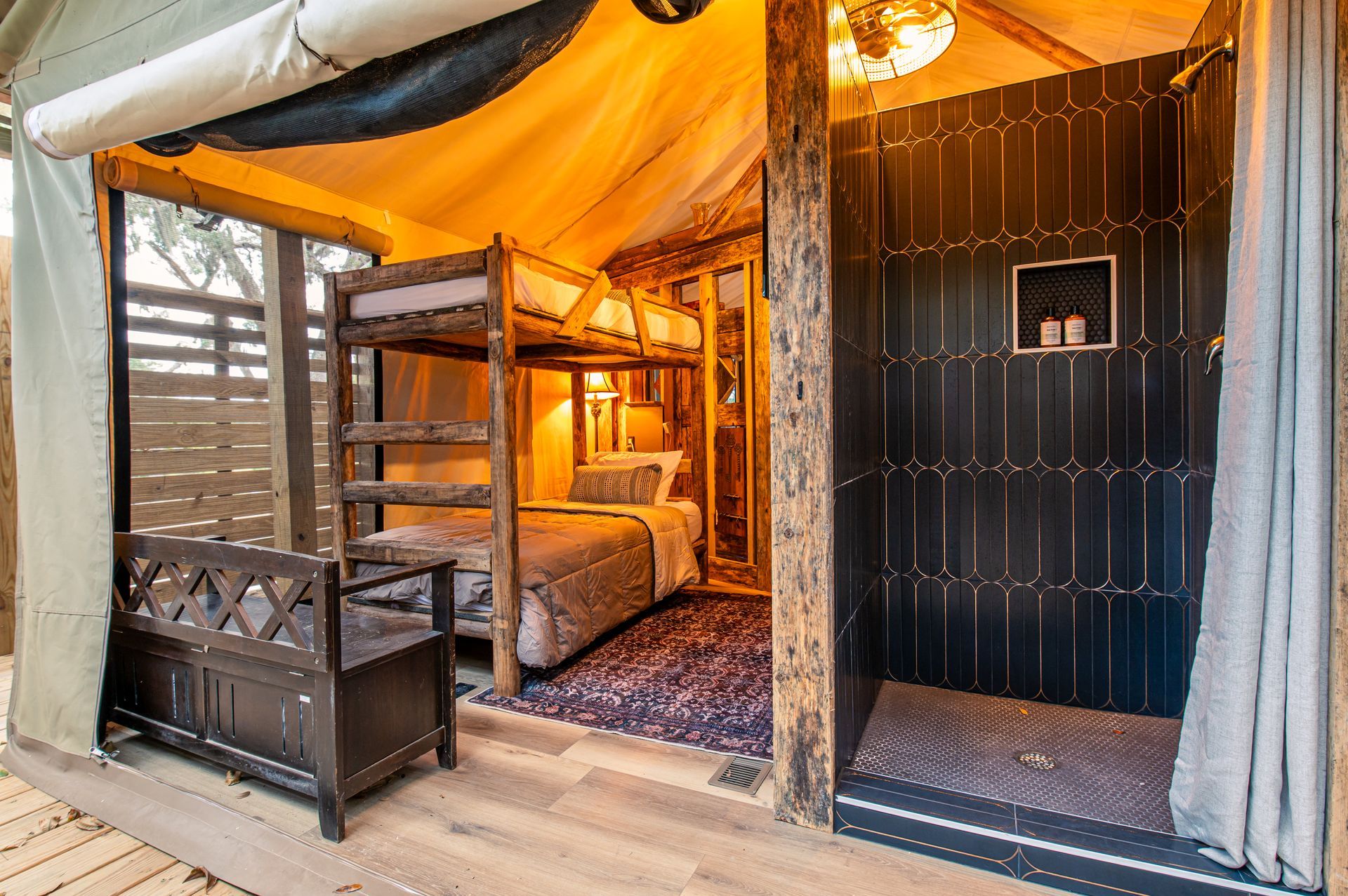 Glamping tent interior with bunk beds, single bed, open shower, and wood furniture.