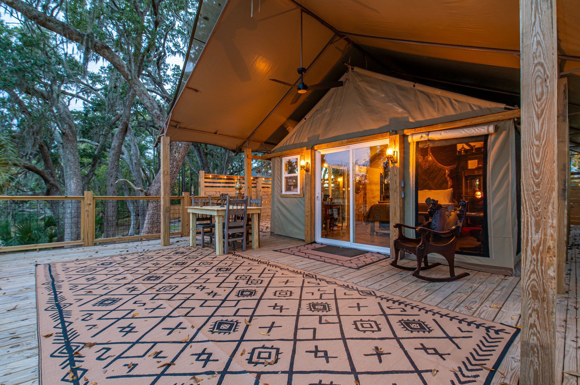 Canvas tent with a porch on a wooden deck. Dining table and rocking chair visible.