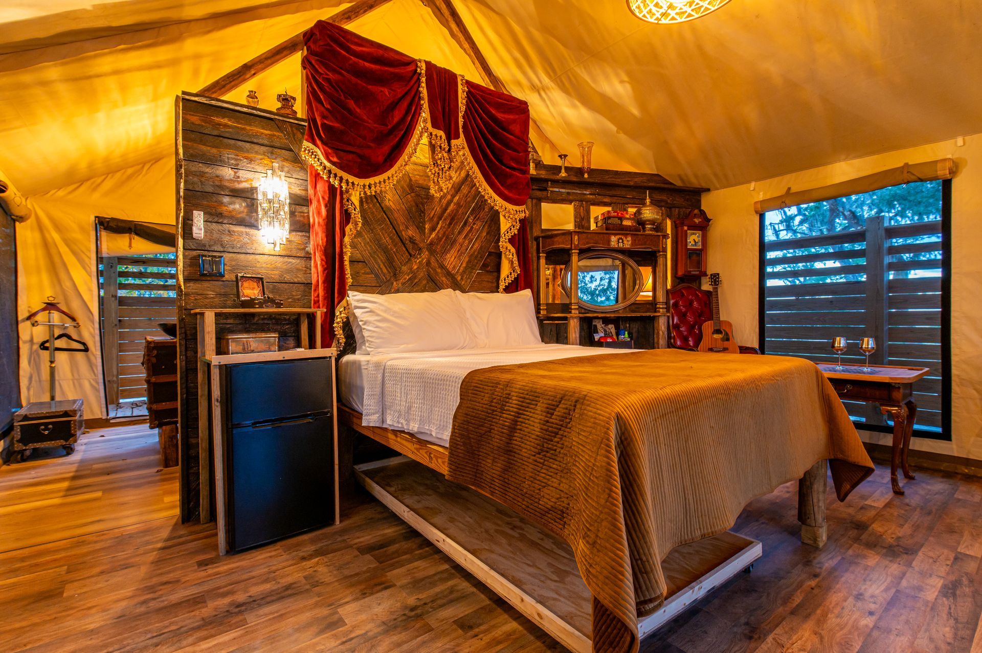 Luxurious glamping tent interior: bed with ornate headboard, draped curtains, and decor.