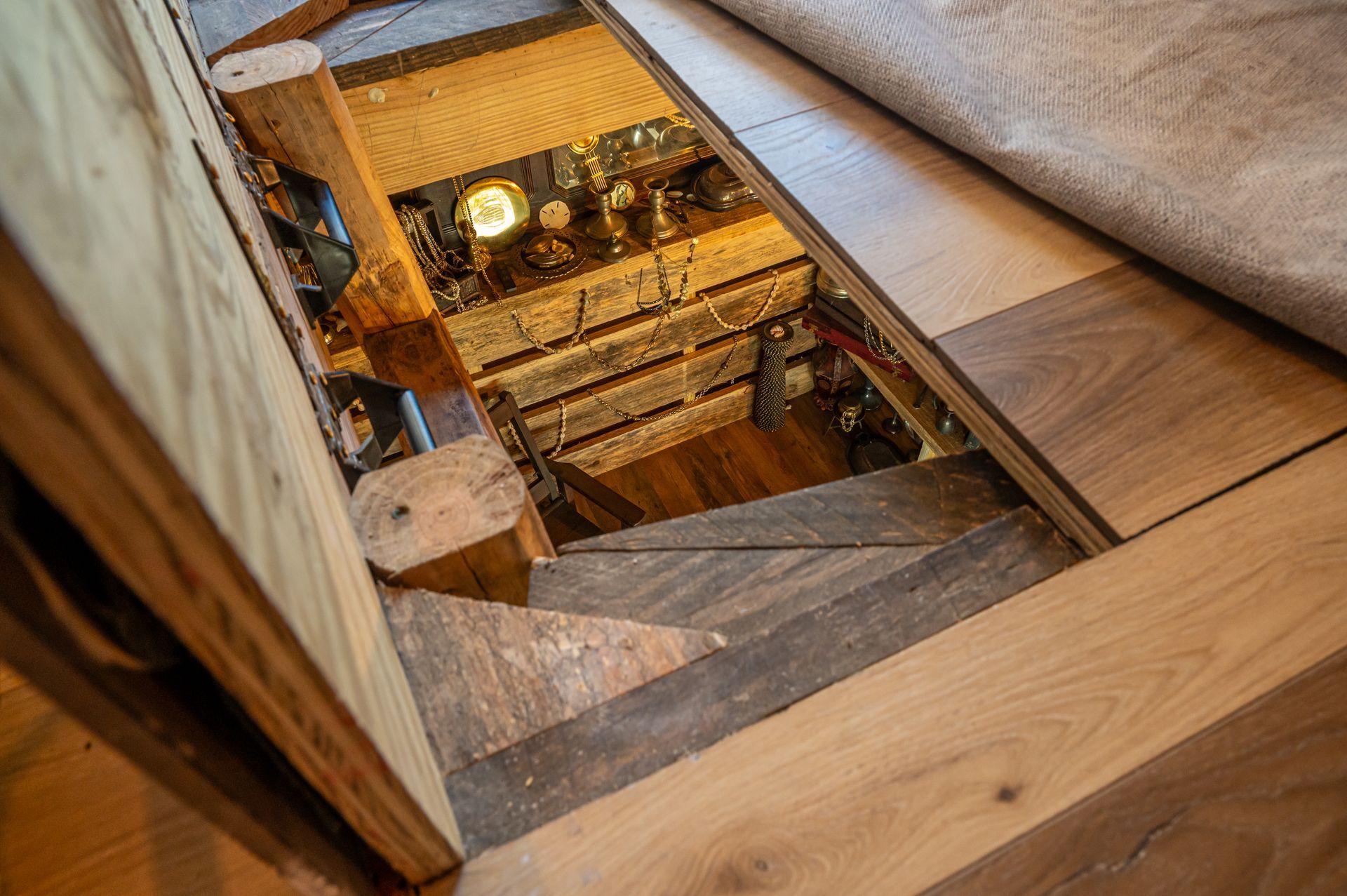 Wooden stairs leading down into a dimly lit space, partially obscured by a partially rolled-up carpet.