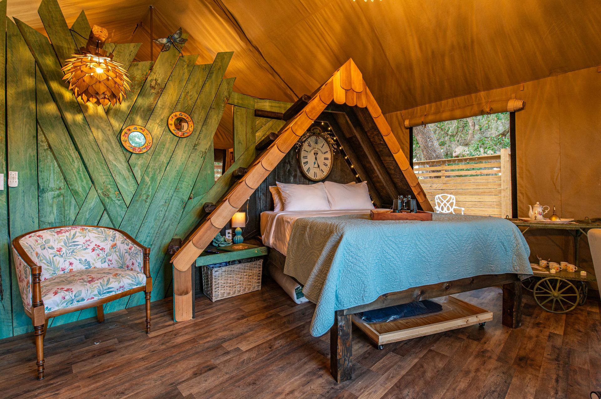Cozy bedroom with wooden accents, bed under peaked roof, floral chair, and a garden view window.