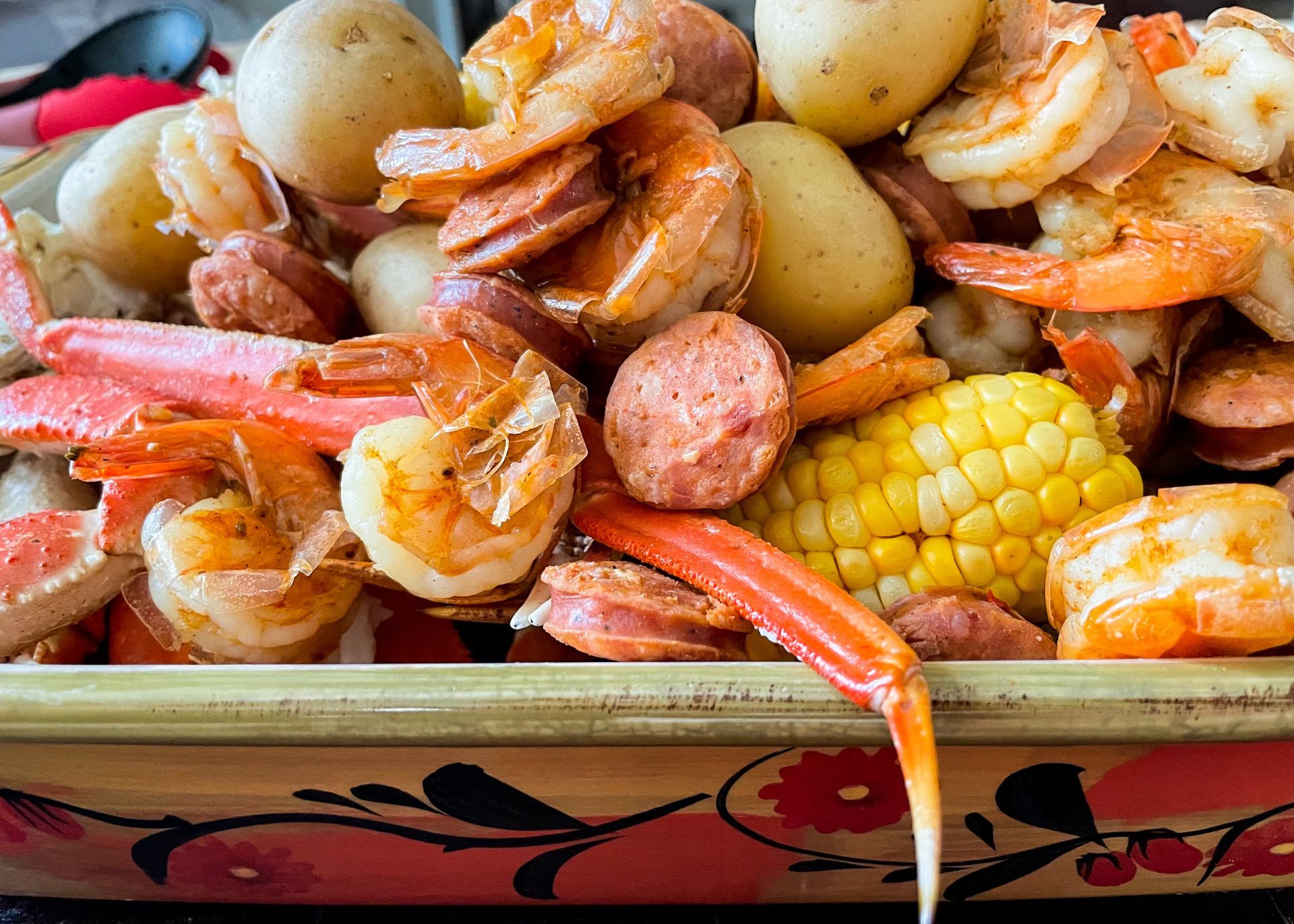 Seafood boil: shrimp, crab legs, sausage, potatoes, corn in a decorative bowl.